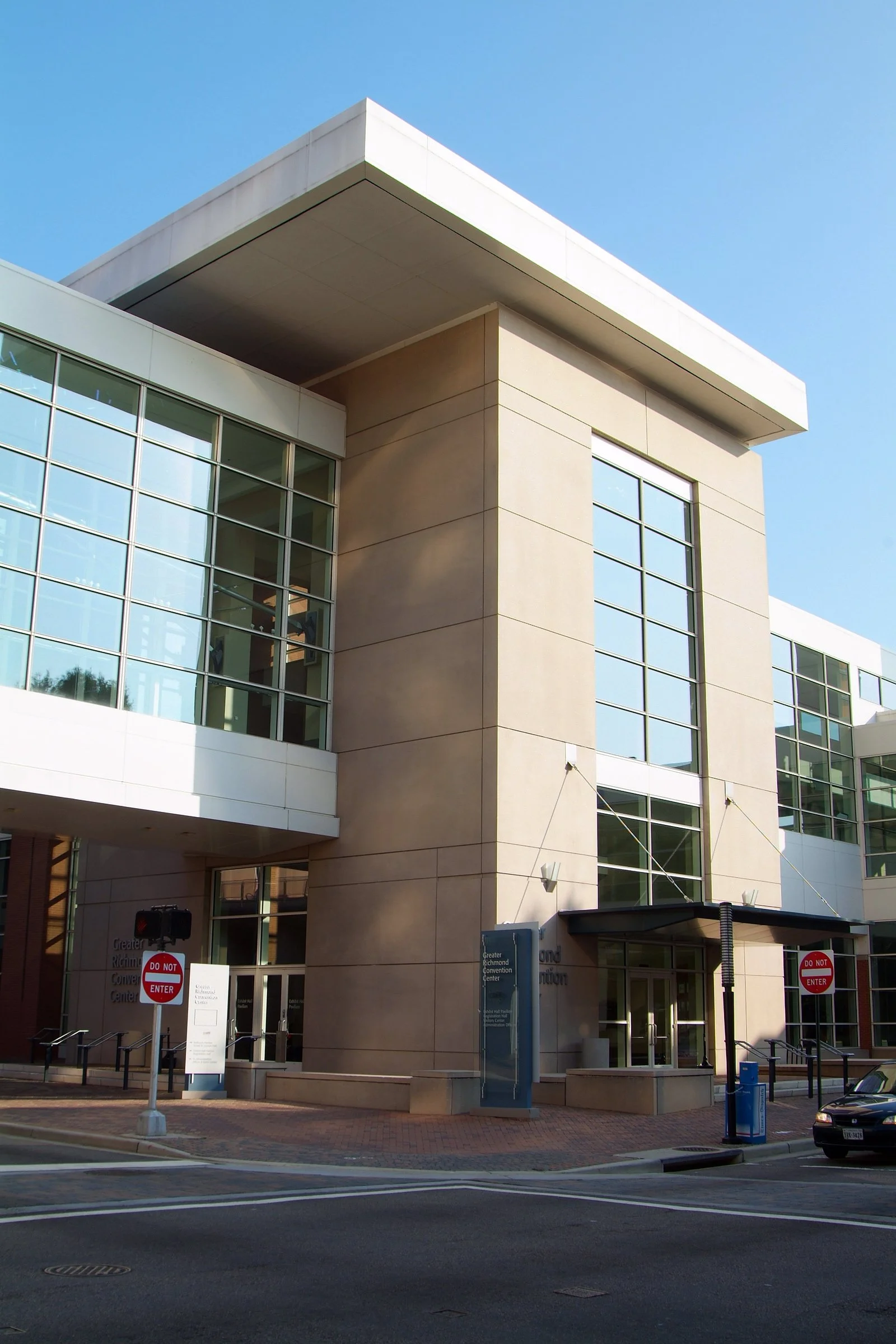 Modern multi-story glass building with beige stone accents and a flat roof, situated at a street corner on a clear day.