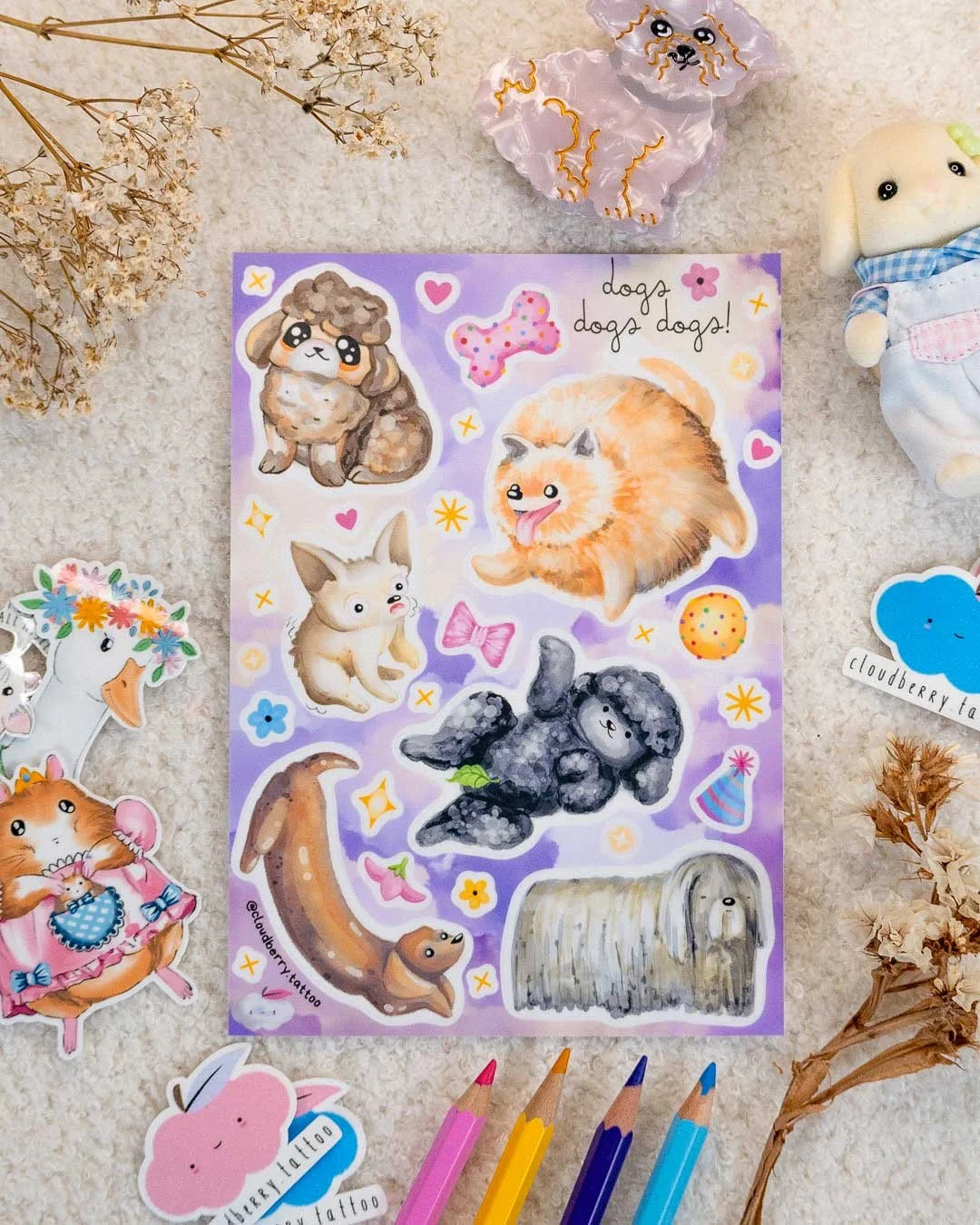 Close-up of stickers featuring cute animals such as a pomeranian, and poodle and other dogs on a purple background, with other artistic materials and paper nearby.
