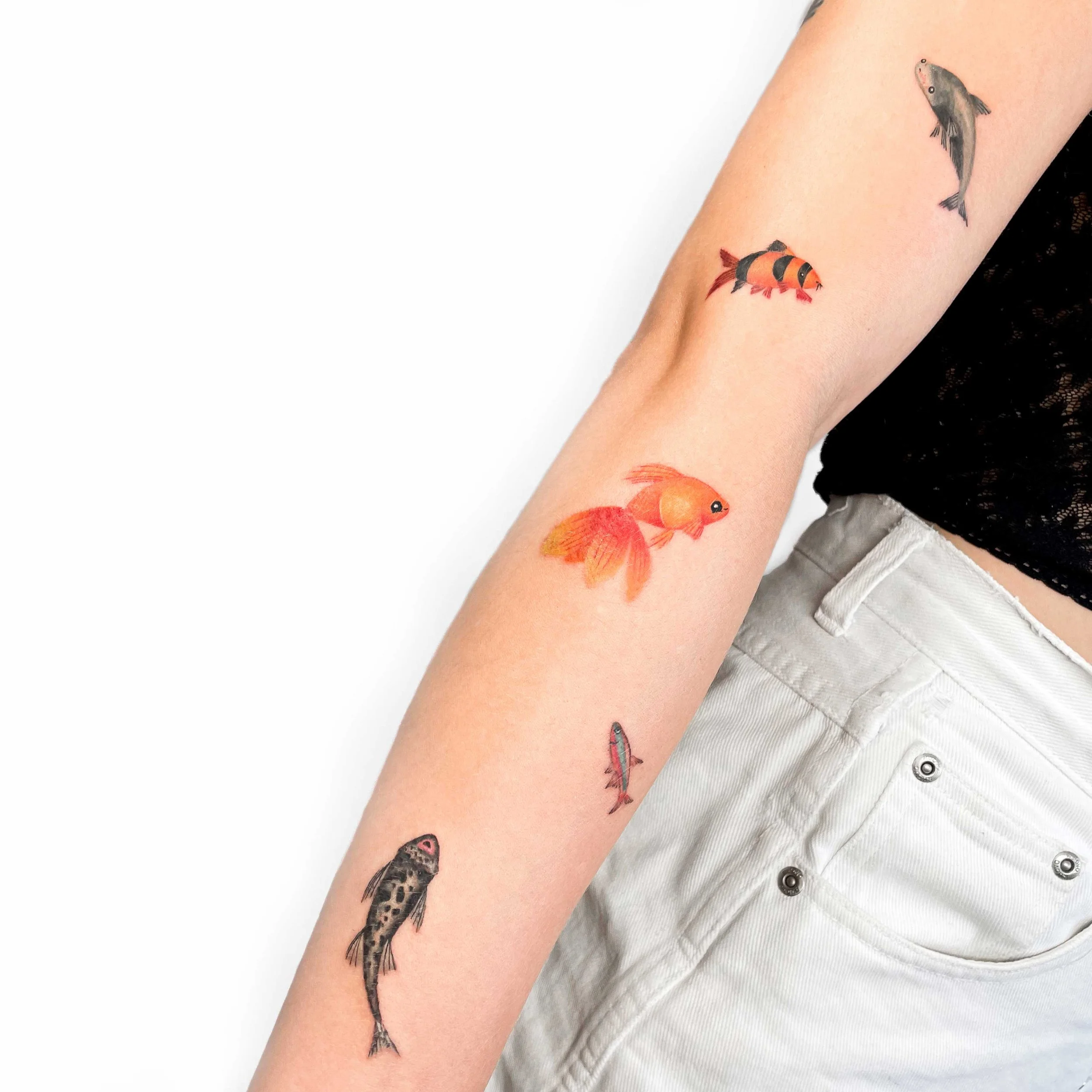 Tattoo of three different fish on an arm, with the fish varying in size and color, including black, orange, and gray.