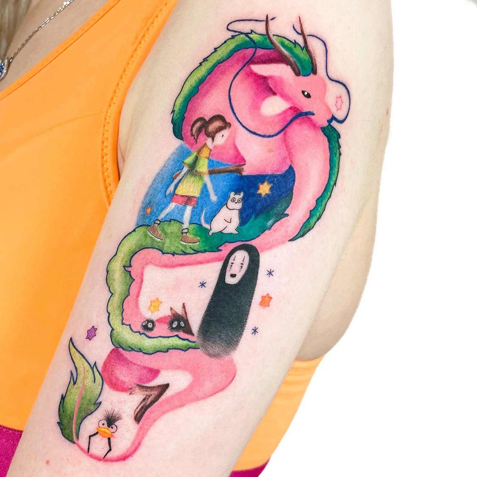Vibrant anime tattoo on a bicep, with Haku dragon and Spirit Away characters in a colorful style.