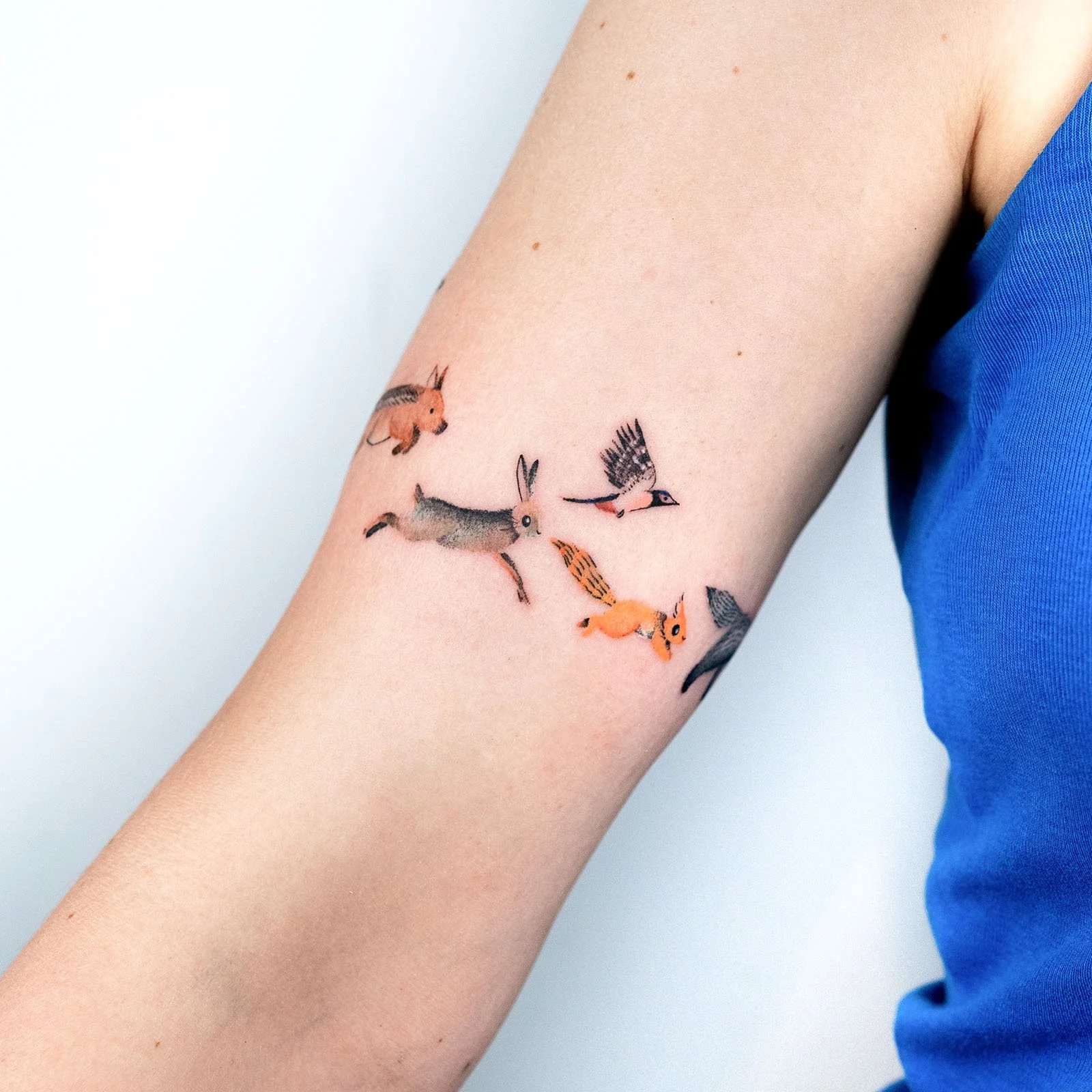Small, colorful forest animals tattoo band on an arm featuring a rabbit, squirrel, and bird.