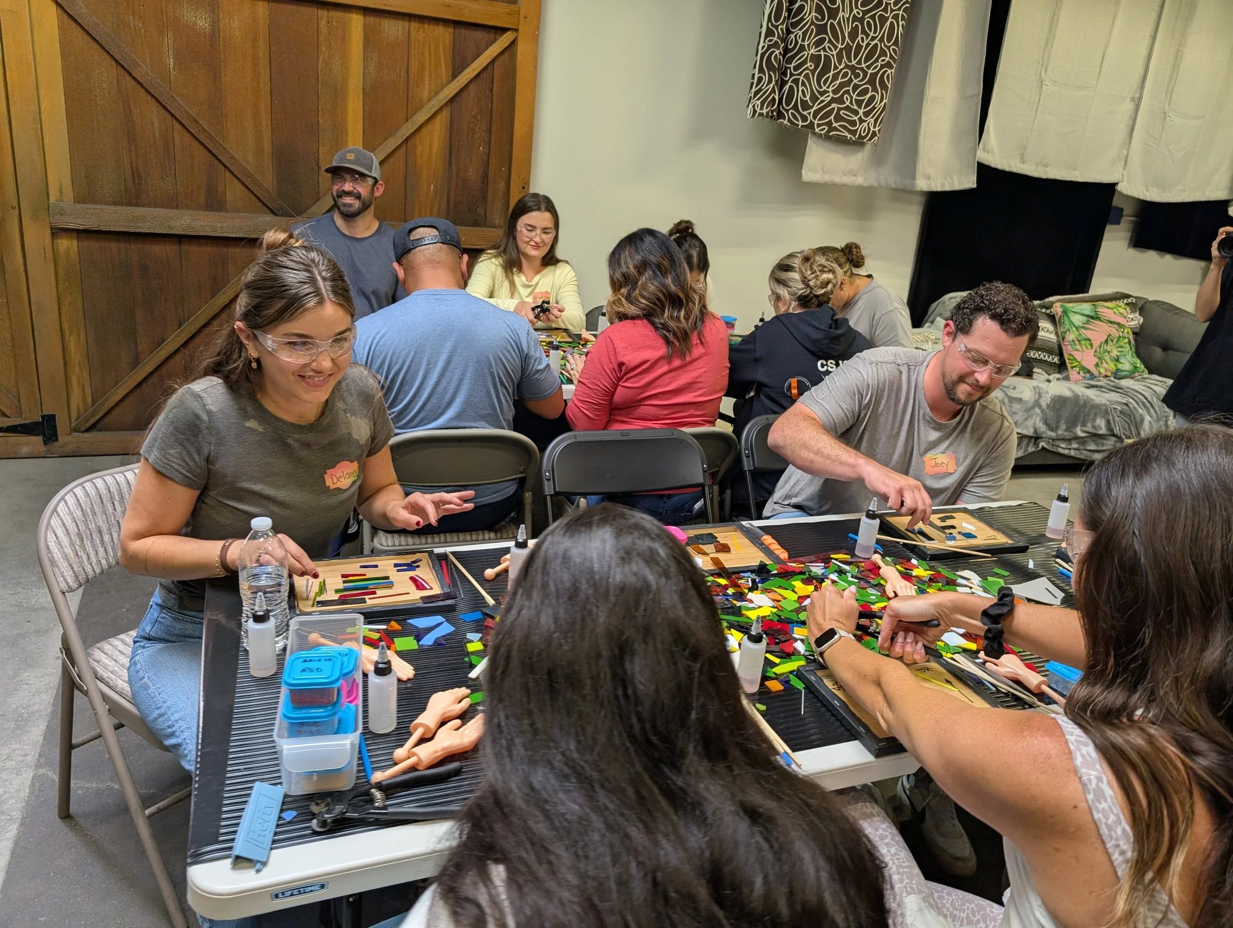 People gathered around tables playing board games in a cozy indoor setting with a wooden sliding barn door and curtains in the background. Teambuilding events for groups.