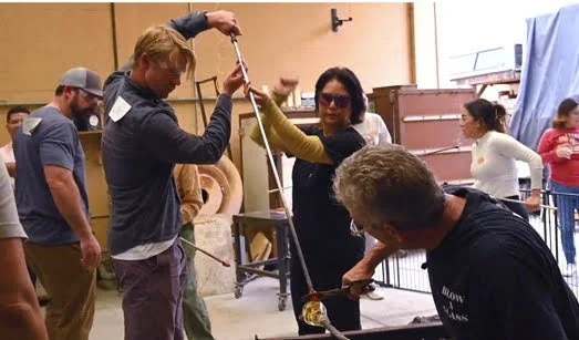 A group of people working together on a glassblowing project in a workshop. Corporate Teambuilding event.