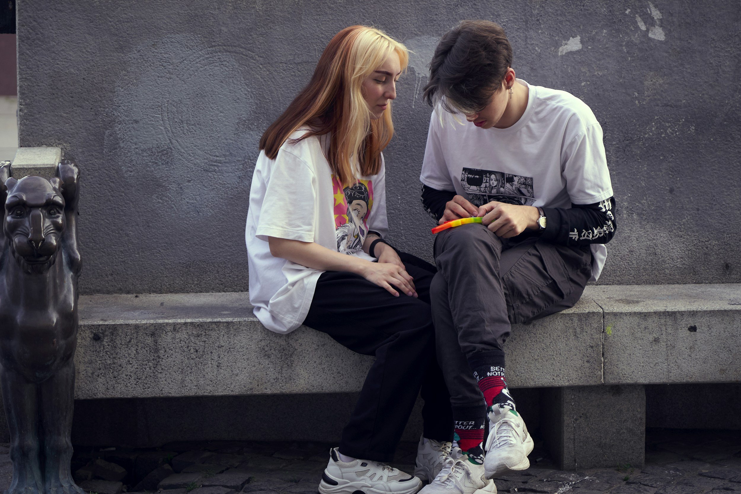 Two teens sit quietly on a bench, one with blonde and brown hair listening as the other holds a fidget toy, reflecting the emotional support and trust built through teen life coaching and mental health support for high school students.