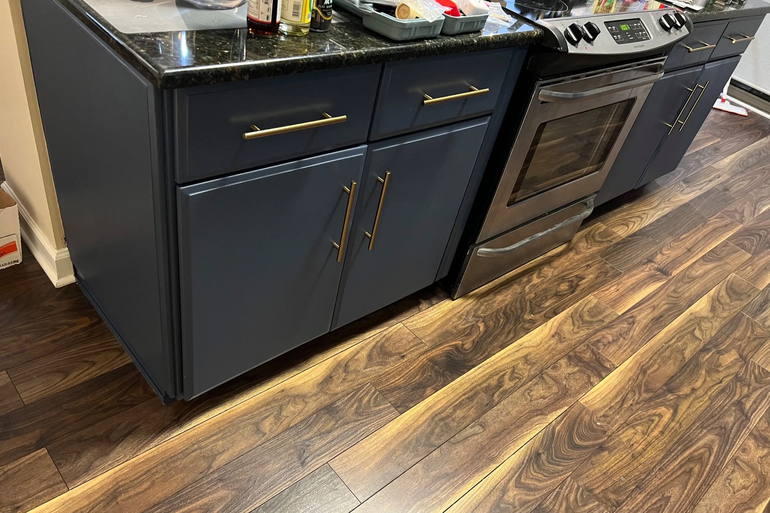 Kitchen with a dark blue cabinet, granite countertop, and stainless steel oven. The floor has wood-like laminate planks with a rich grain pattern.