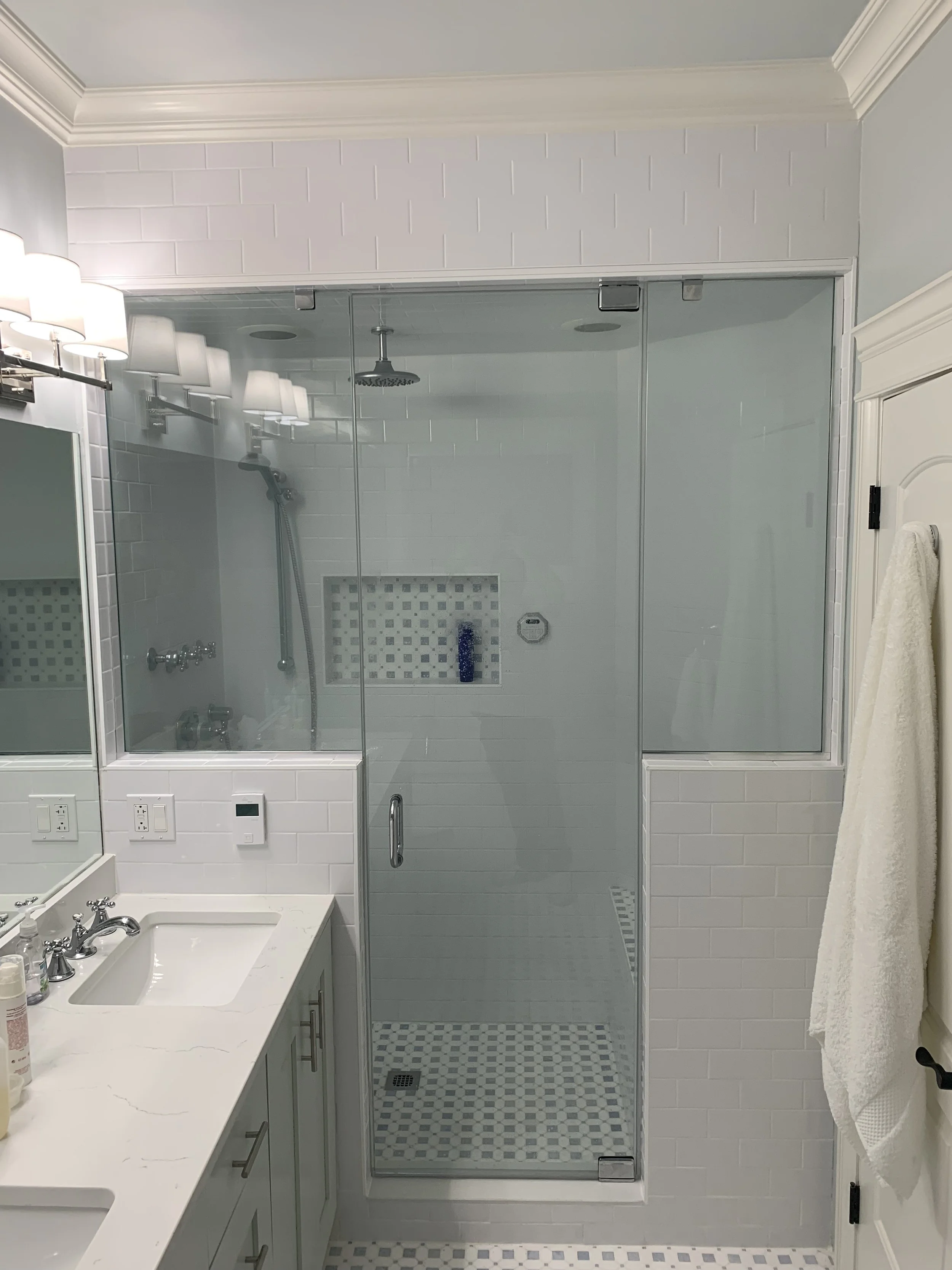 Bathroom with a glass shower enclosure, white subway tile, a built-in shower niche with shampoo bottles, a white vanity with a sink, and a towel hanging on a hook.