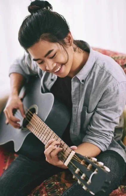 Man smiling while playing guitar representing reconnecting with daily life after healing from PTSD related to childhood trauma