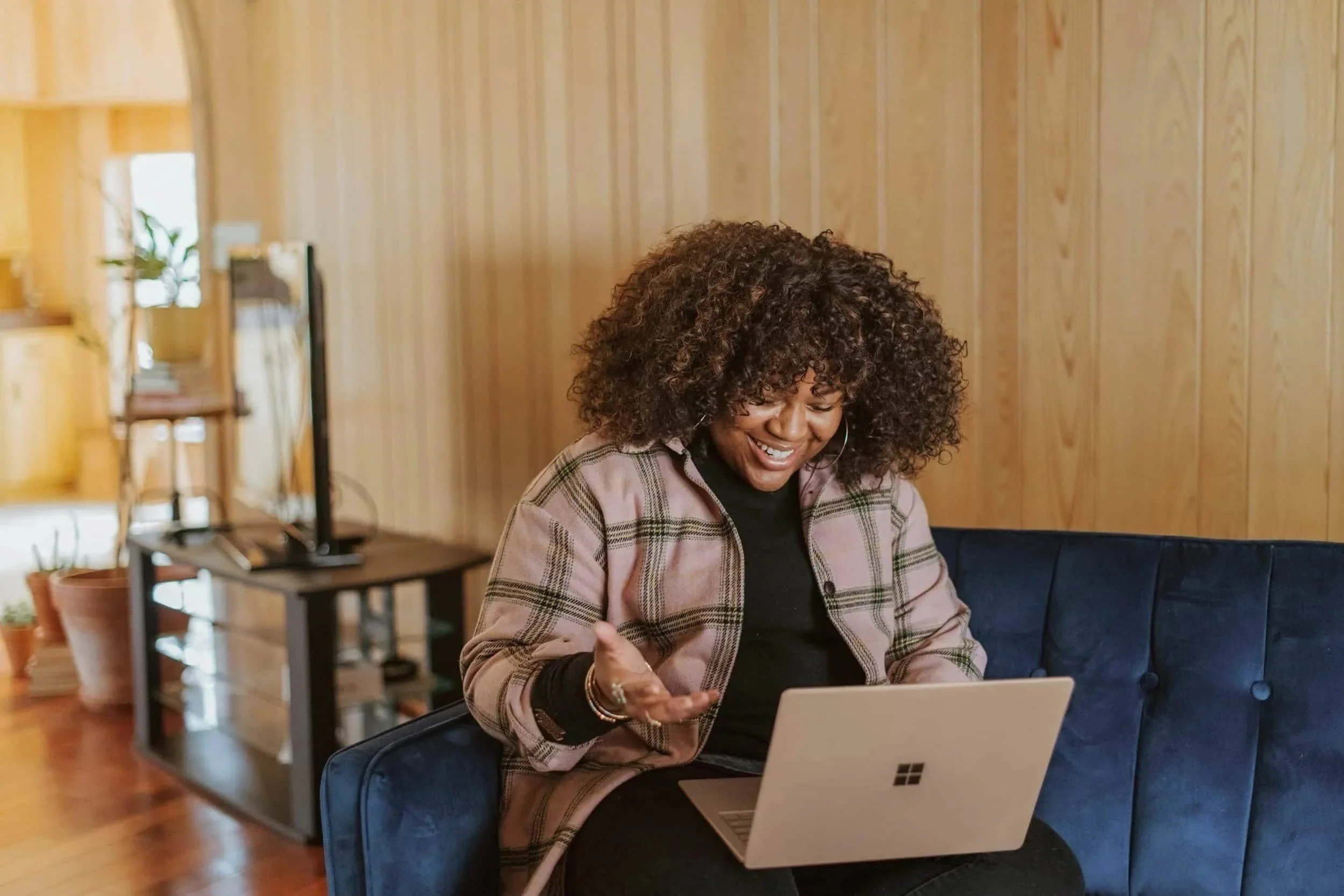 Smiling woman sitting on a couch with her laptop, appearing to engage in virtual therapy from home in Pennsylvania or Delaware.