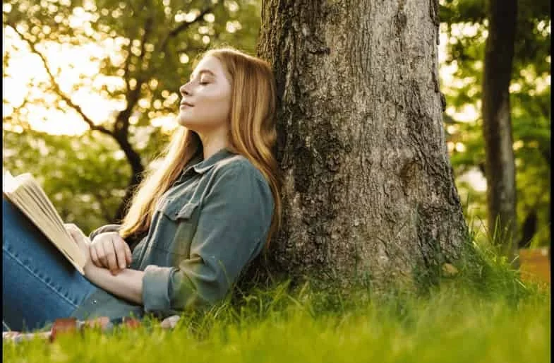 Woman resting against a tree with eyes closed, reflecting calm and nervous system regulation during childhood trauma healing