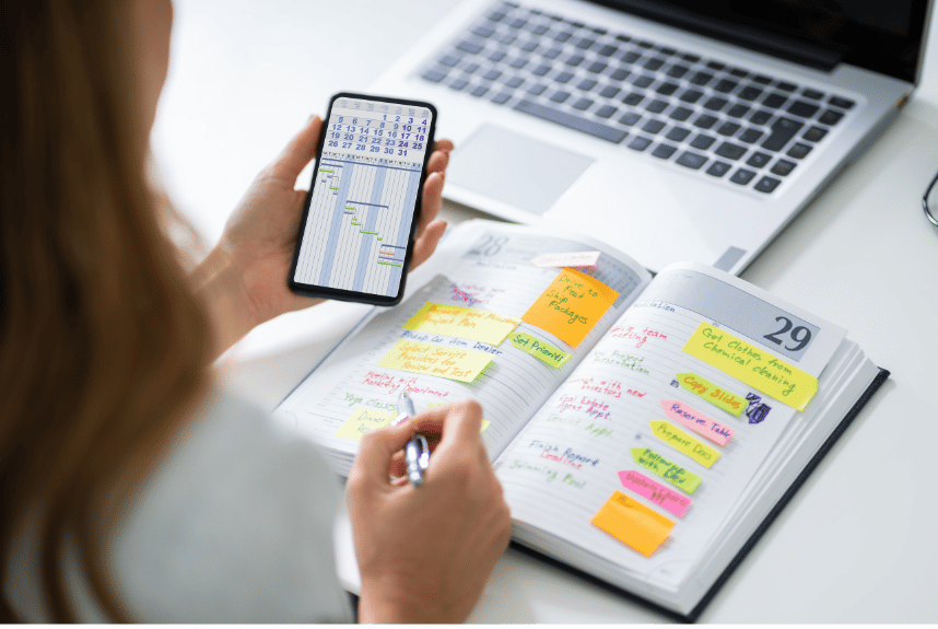 Woman looking at her phone calendar while sitting at a desk with a planner, reflecting emotional overwhelm and constant responsibility connected to childhood trauma