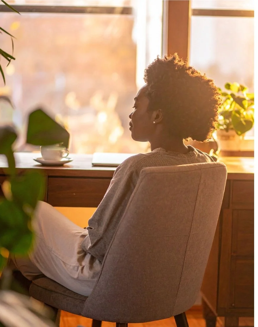 Woman sitting quietly by a window reflecting, representing how childhood trauma can shape feelings of being a burden in adulthood