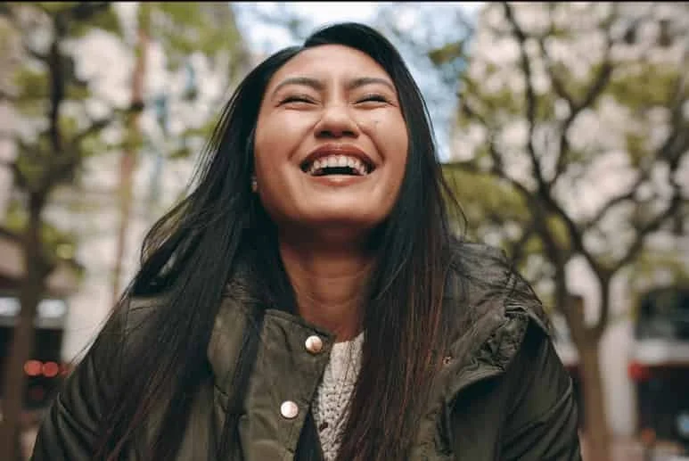 Millennial woman smiling and laughing outdoors, representing emotional relief and a sense of peace after trauma therapy.