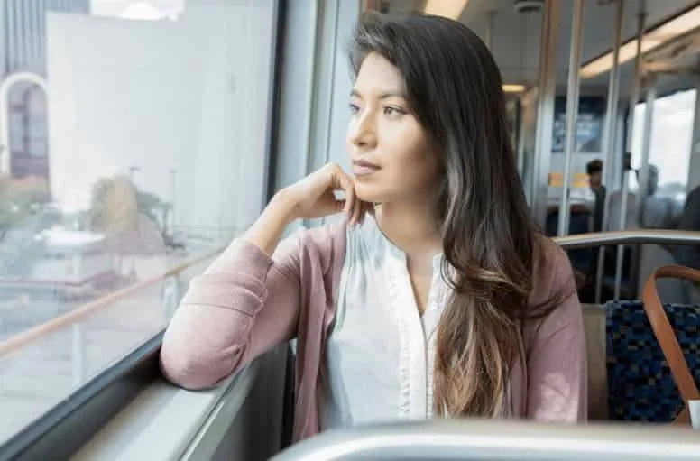 Woman sitting on a train looking tired and reflective, representing trauma-related exhaustion despite maintaining daily responsibilities.