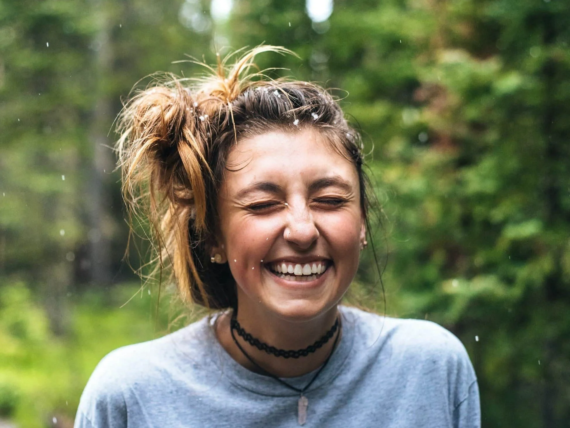 Close-up of a young adult smiling with eyes closed in a green forest—feeling safer and calmer after trauma therapy in Bryn Mawr & Newark, DE.