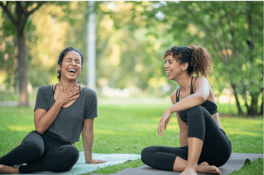 Two millennial women laughing together outdoors, representing connection and emotional wellbeing after trauma therapy.