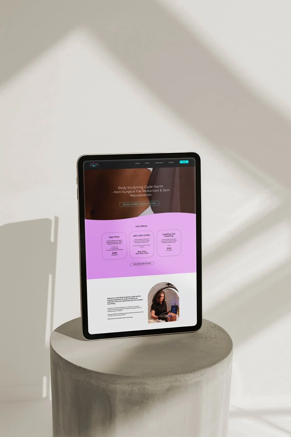 Freelance Graphic Designer Melbourne. An iPad displaying a website for body sculpting services, placed on a cylindrical concrete pedestal against a white wall with shadows.