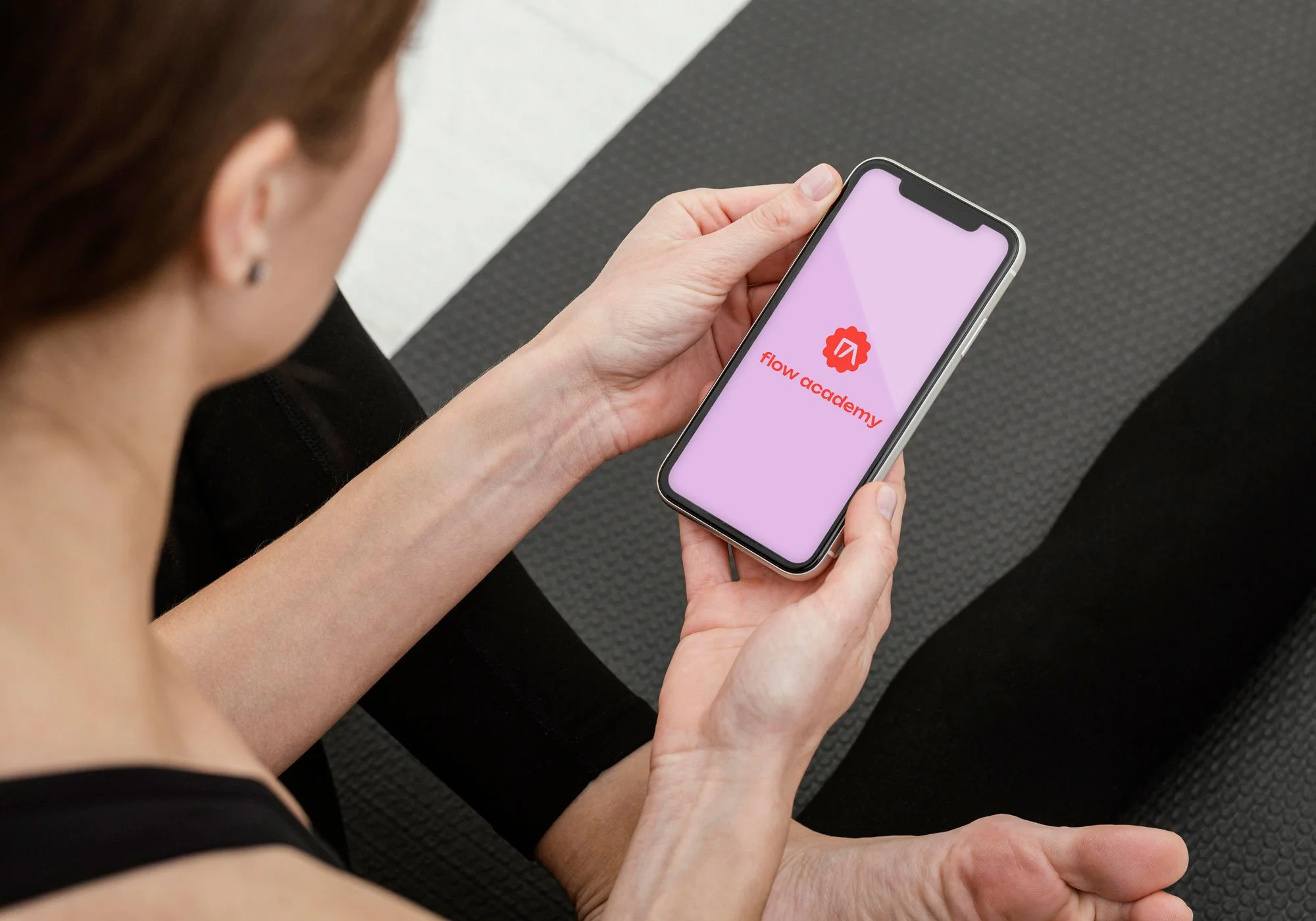 Freelance Graphic Designer Melbourne. A woman holding a smartphone displaying the Flow Academy logo and name on a pink background.