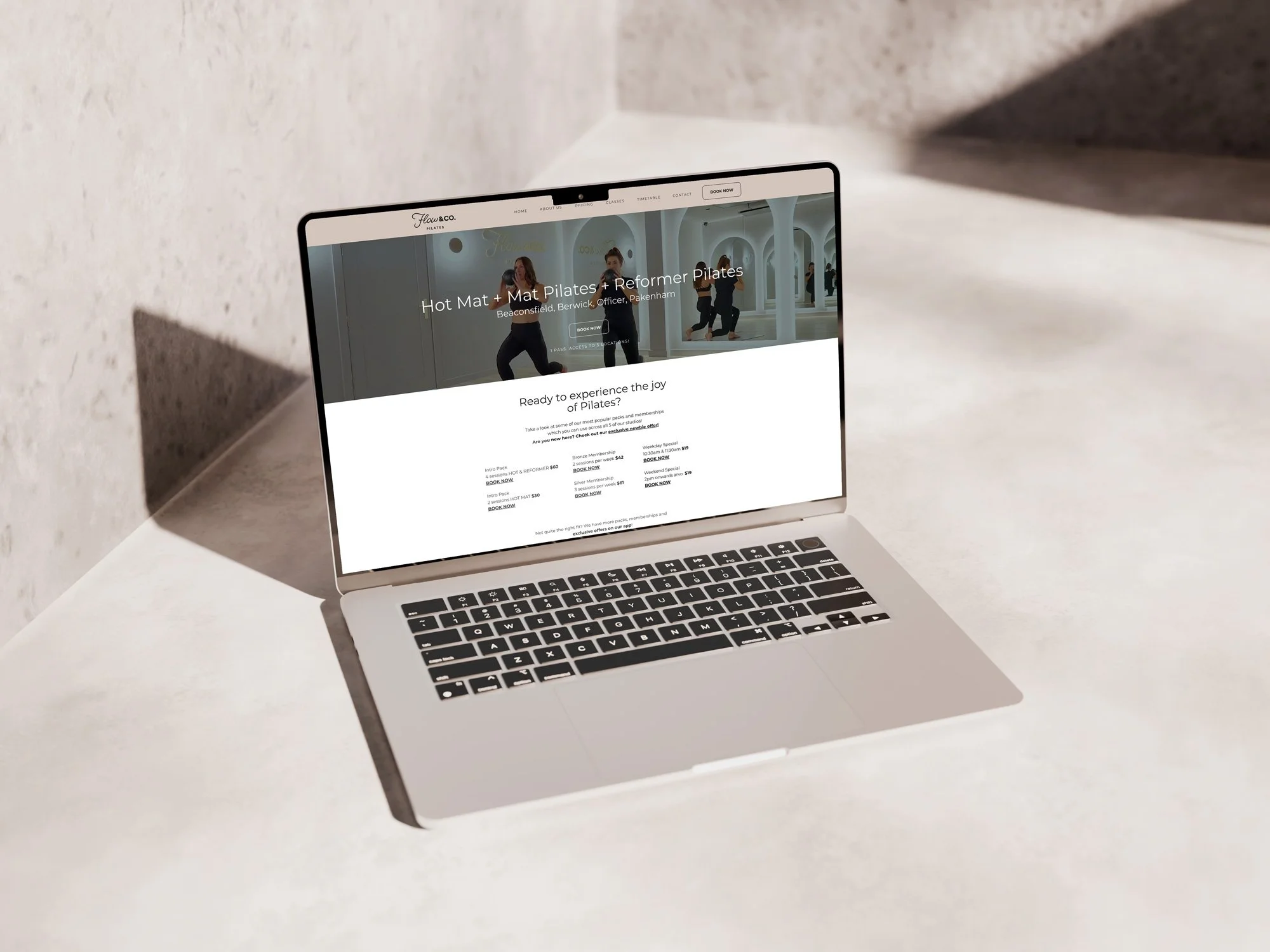 Open MacBook laptop on a white surface showing a website for a Pilates class.