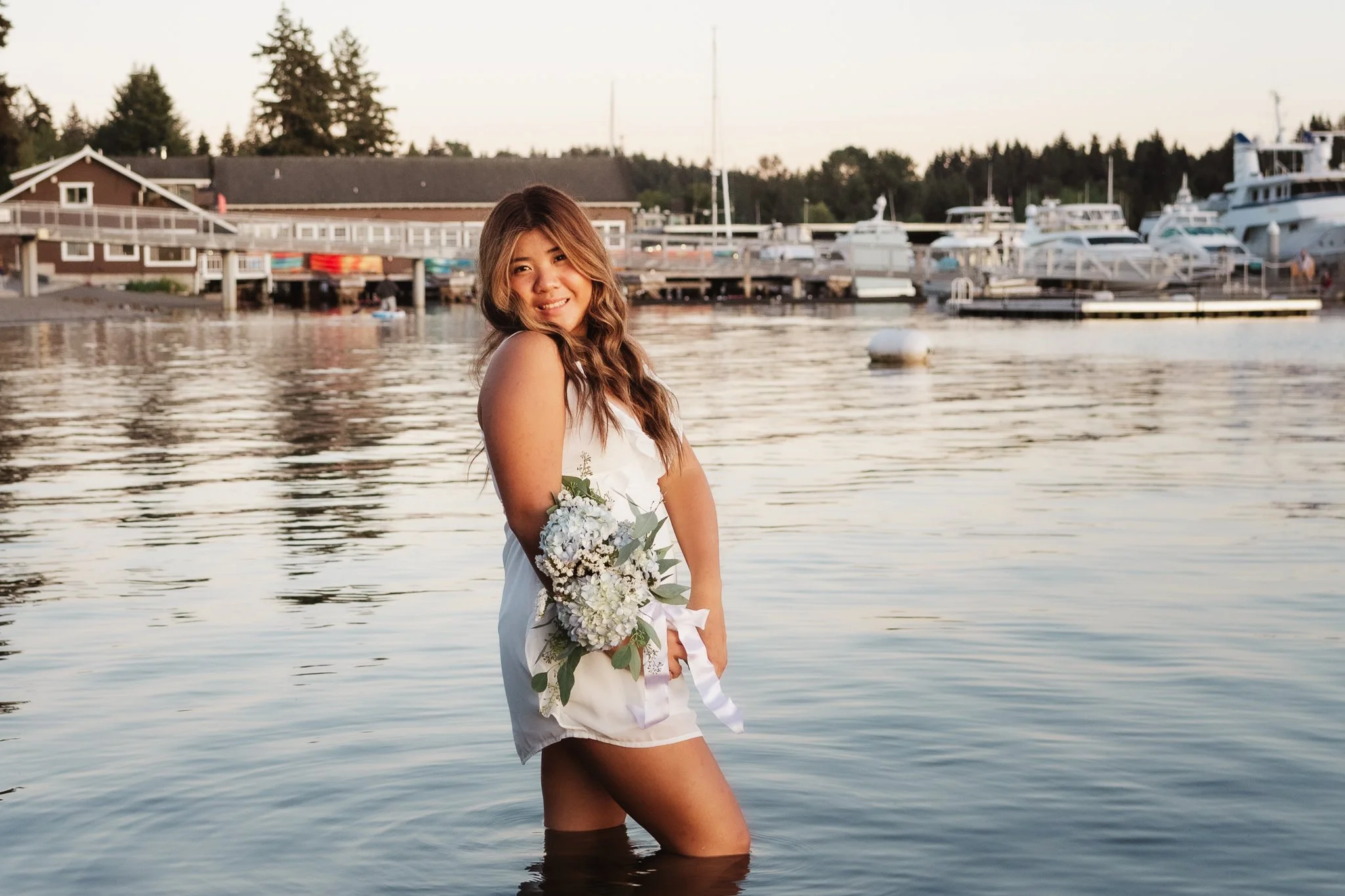 A high school senior girl standing in water during golden hour sunset at Meydenbauer Bay Park in Bellevue having her photos taken by Cindy Richey Photography