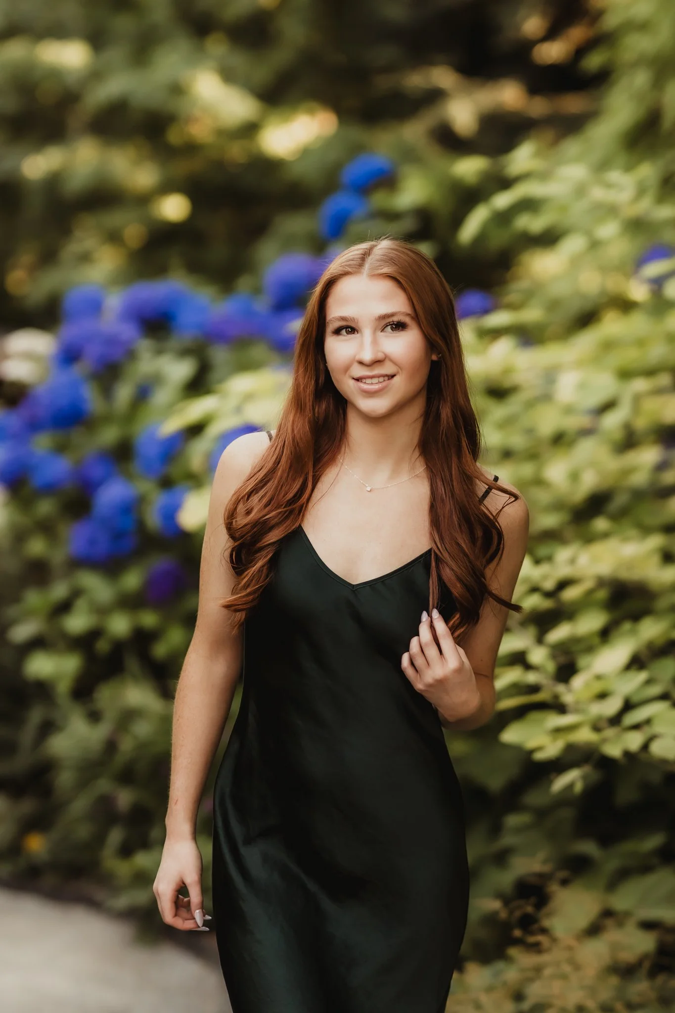 A high school senior girl posing in a black dress with blue hydrangeas at Bellevue Botanical Garden during senior photos taken by Cindy Richey Photography.