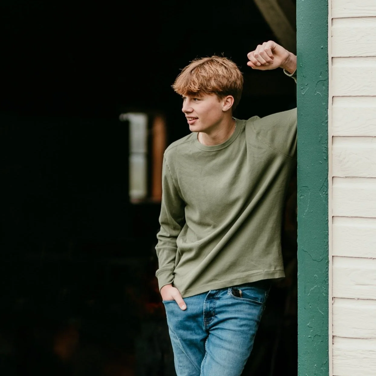 A high school senior guy posing in the doorway of a barn near Issaquah, wearing a green shirt and jeans having his senior photos taken by Cindy Richey Photography.