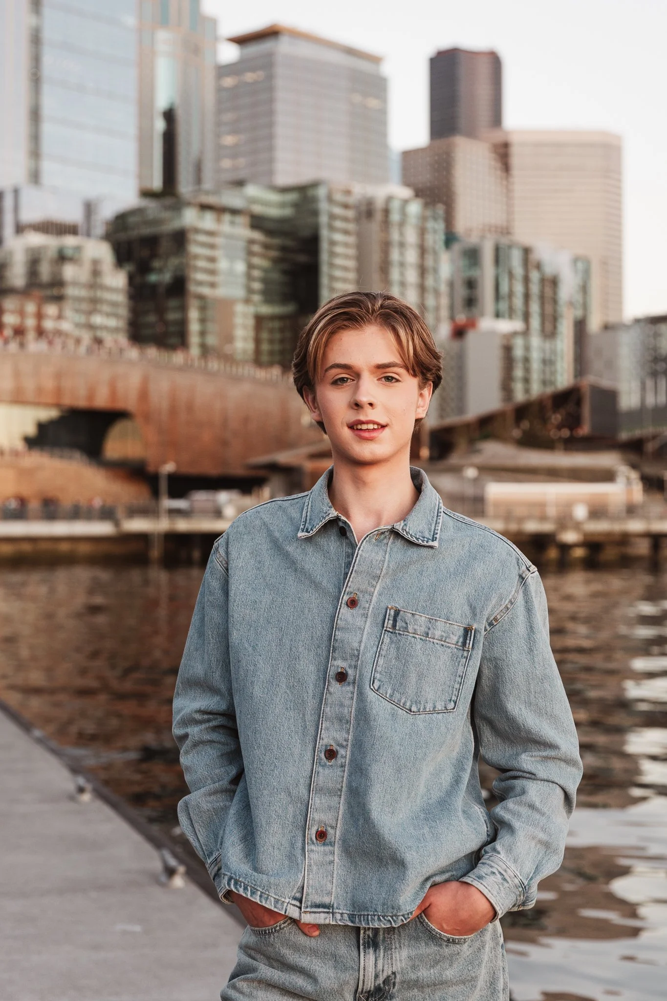 A senior guy at the Seattle waterfront during golden hour, wearing a denim shirt and jeans during a portrait session with Cindy Richey Photography