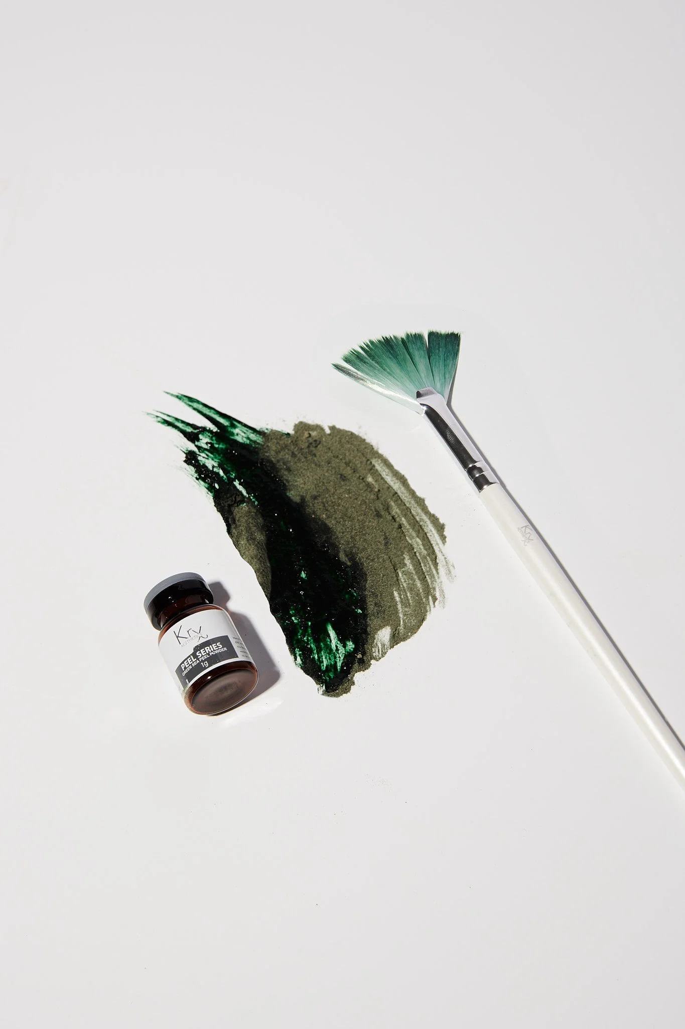Nail dip powder container, green nail dip powder, and a fan-shaped nail brush on a white background.