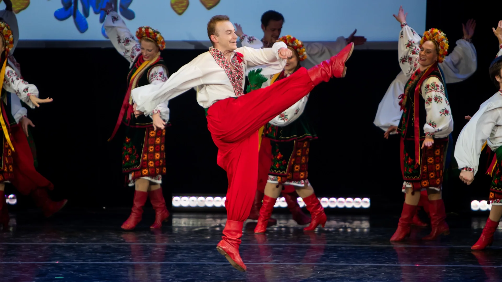 Rusalka Ukrainian Dance Ensemble male performer executing a high kick during a traditional Ukrainian dance, surrounded by dancers in embroidered folk costumes on stage in Winnipeg