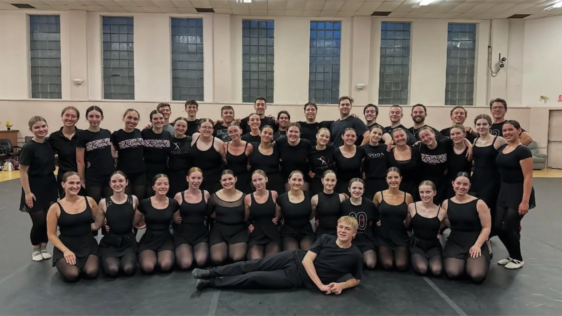 Large group photo of Rusalka dancers in black outfits gathered in a gym setting.