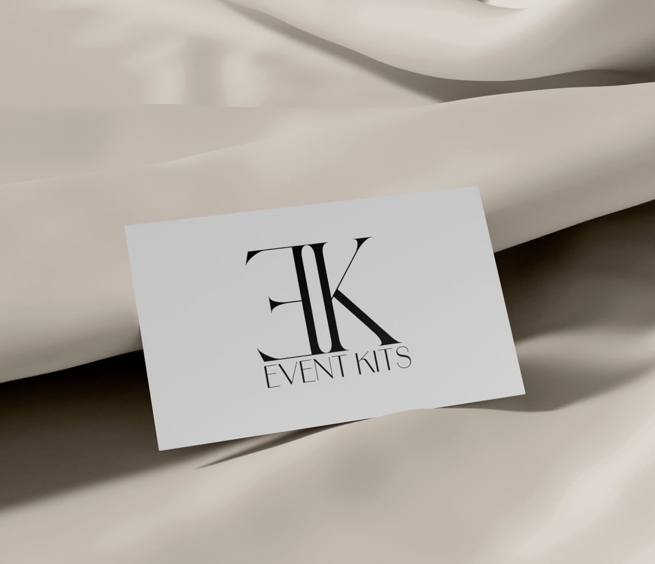 A white card with black lettering reading 'EK Event Kits' placed on a cream-colored fabric background.