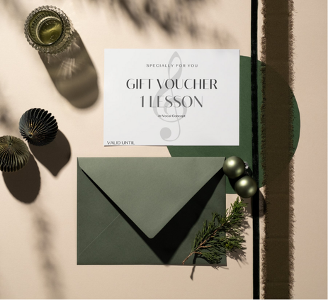A gift voucher for one lesson placed on top of a green envelope, surrounded by holiday decorations including gold and black ornaments, a sprig of evergreen, and a small glass jar, with sunlight casting shadows.