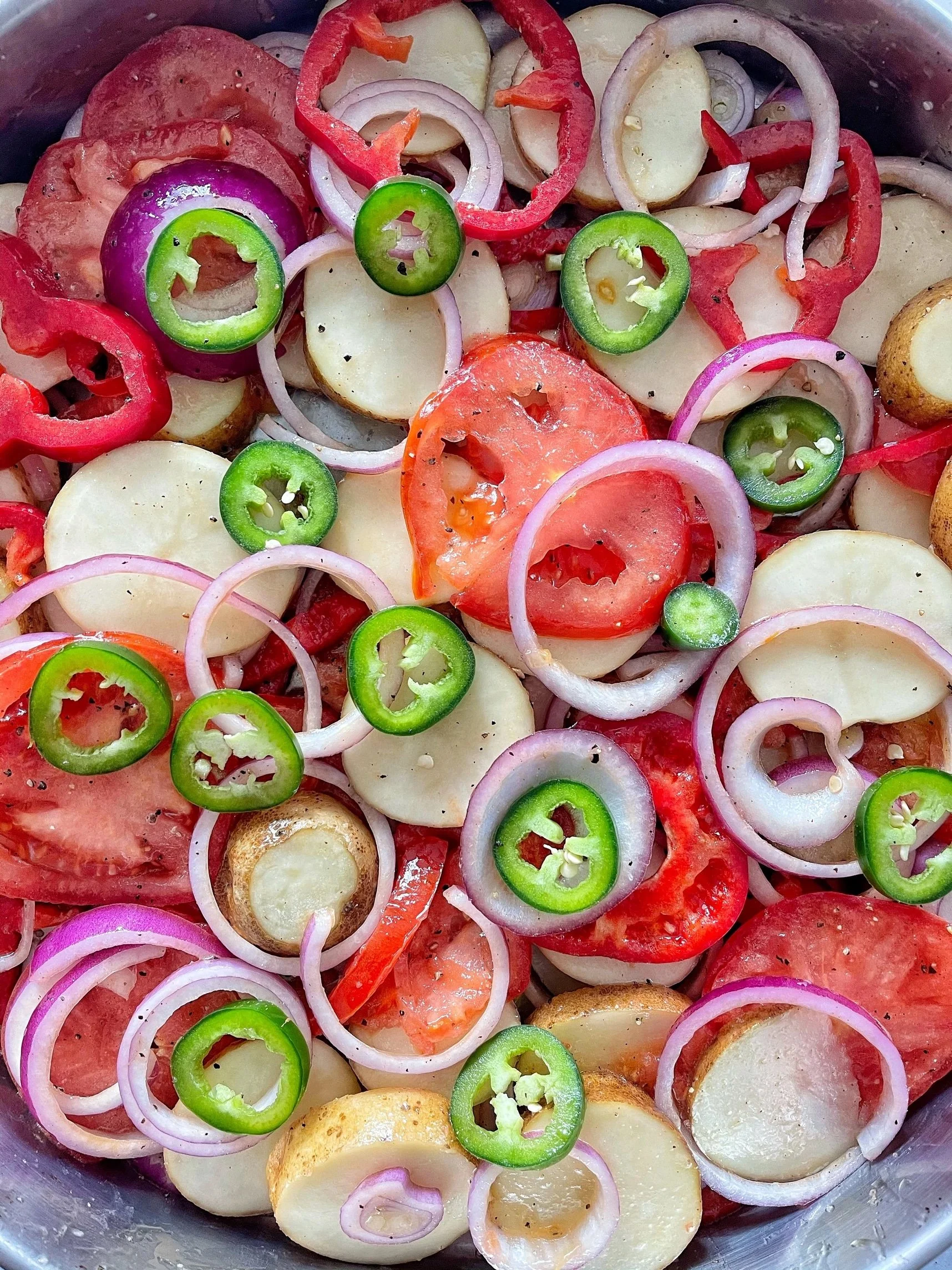 Sliced tomatoes, onions, potatoes, red bell peppers, and jalapeños in a bowl.