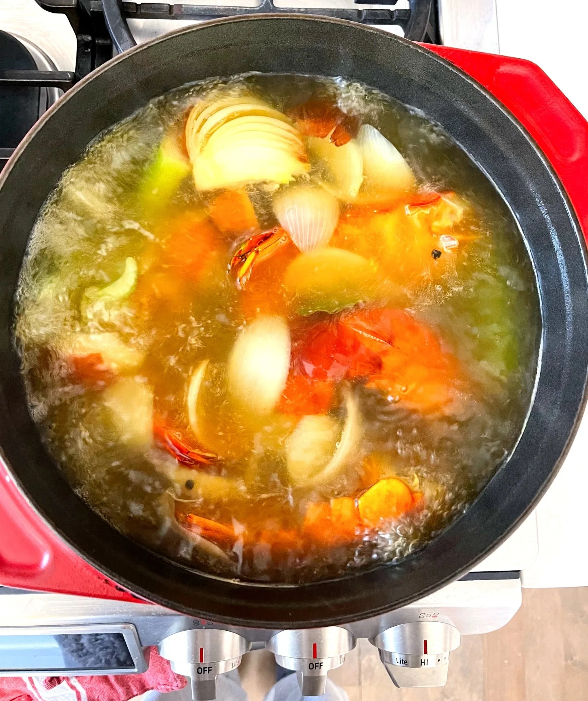 Pot of boiling water with onions, carrots, celery, and lobster shells for stock preparation.