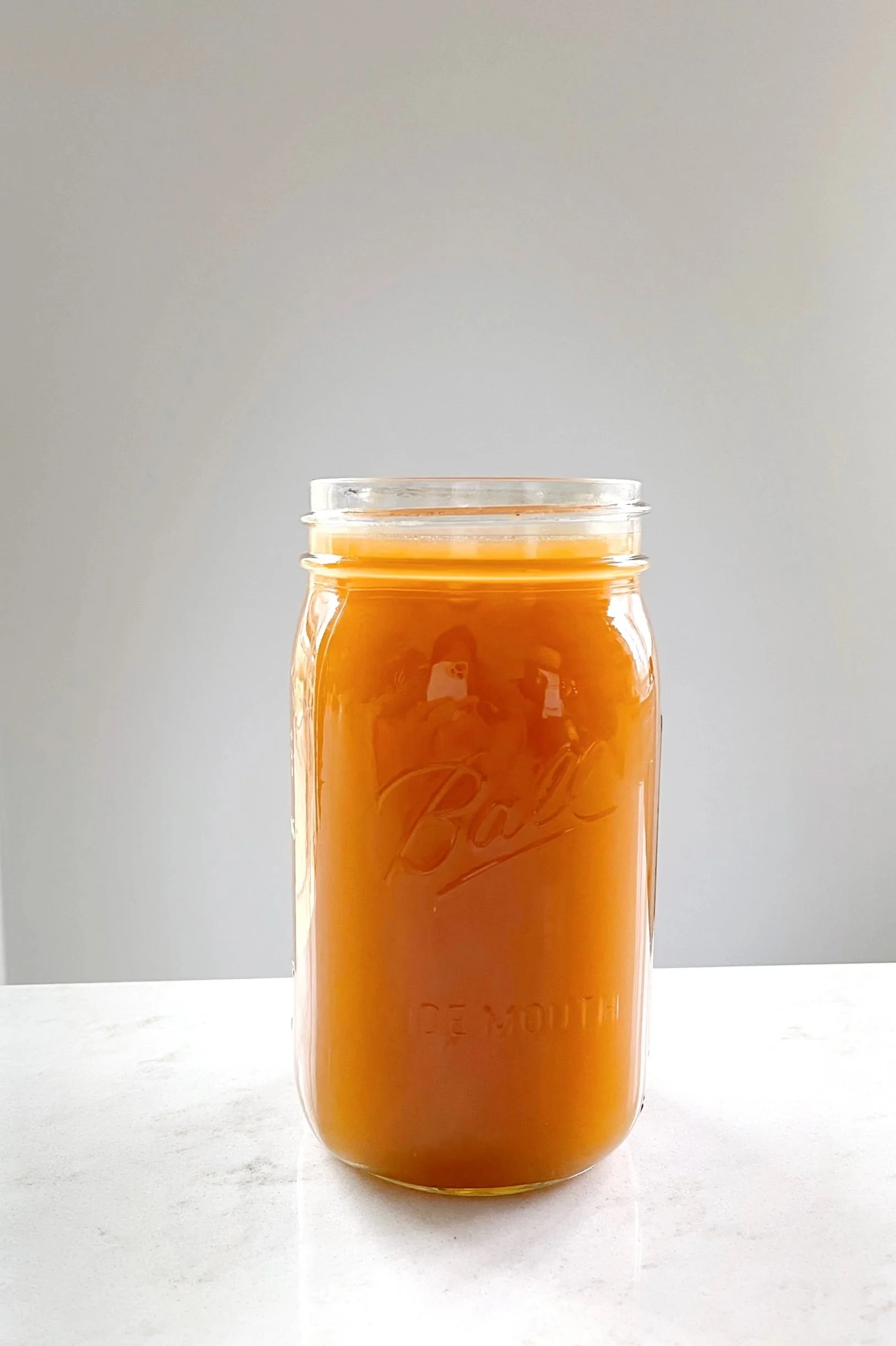 Glass jar filled with orange liquid, possibly juice, on a marble surface.
