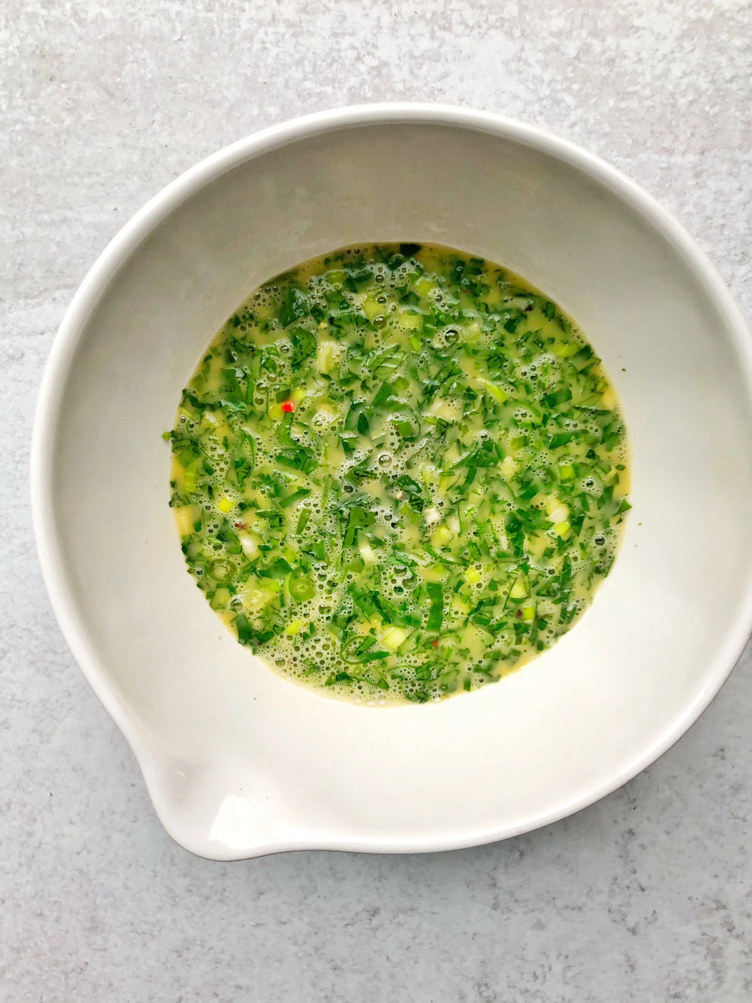 Bowl of green liquid with chopped herbs on a gray surface.