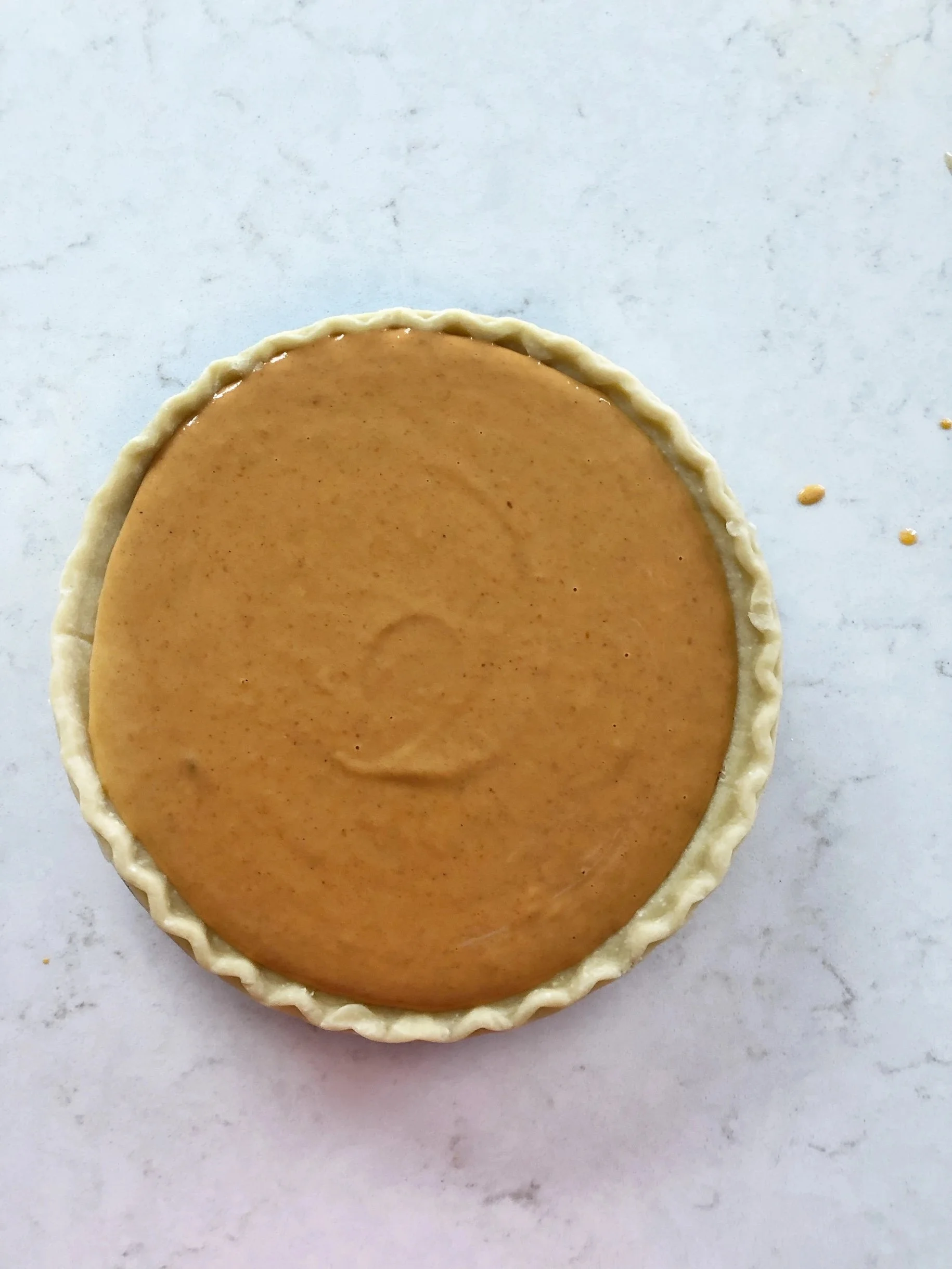 Unbaked pumpkin pie with a crimped crust on a light marble surface.