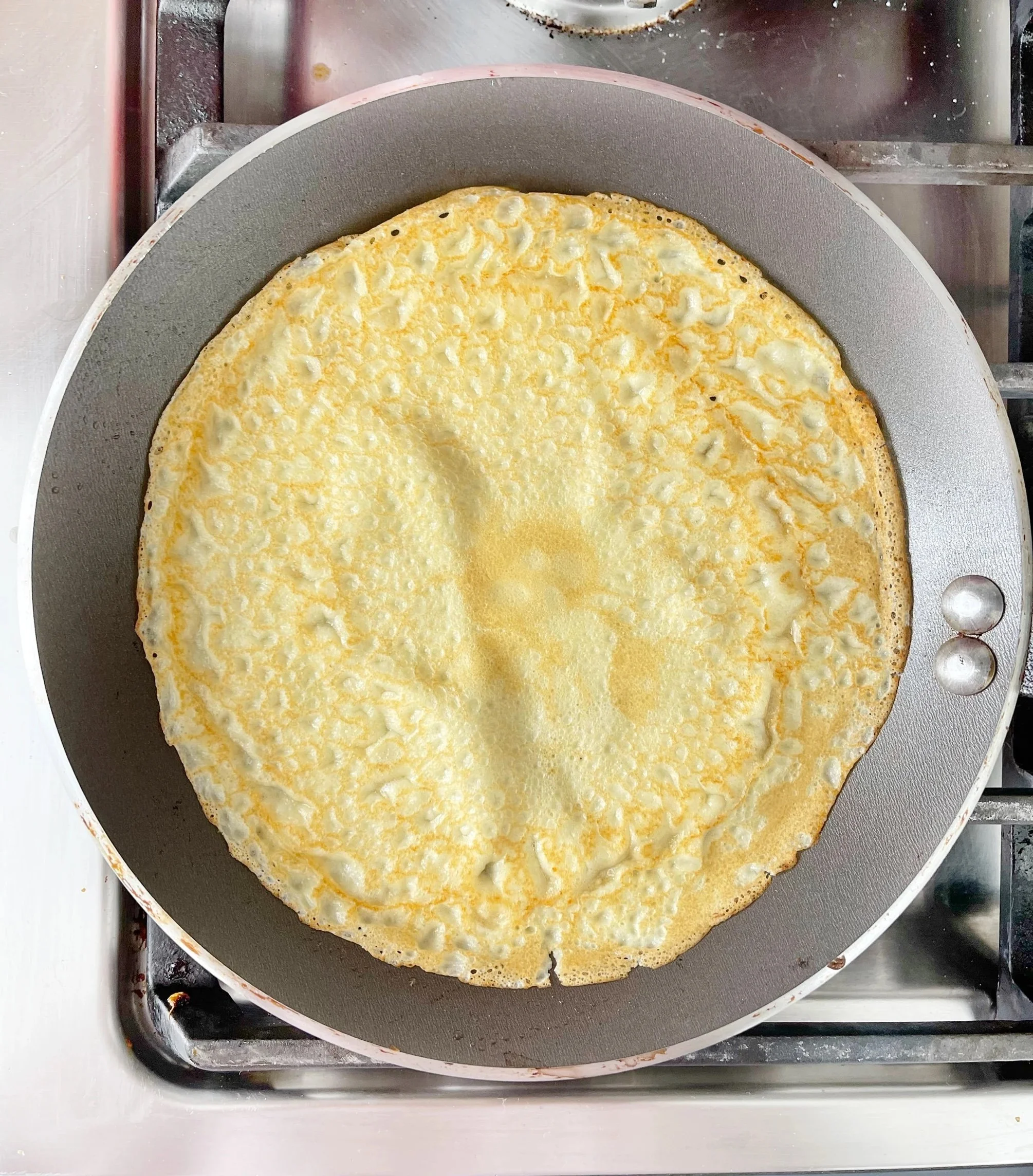 A crepe cooking in a non-stick frying pan on a stove.