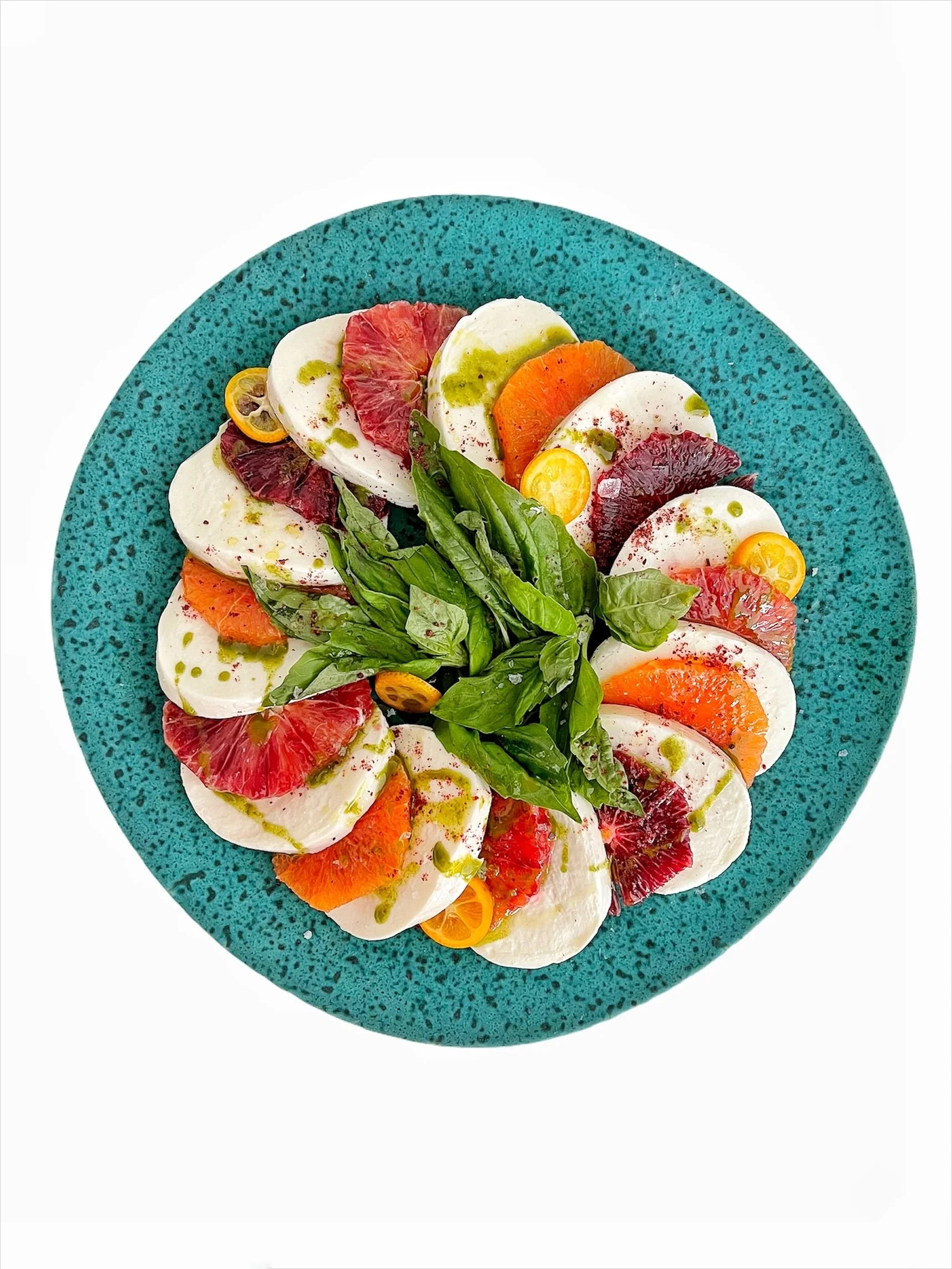 Caprese salad with mozzarella, citrus slices, and basil on a turquoise plate.