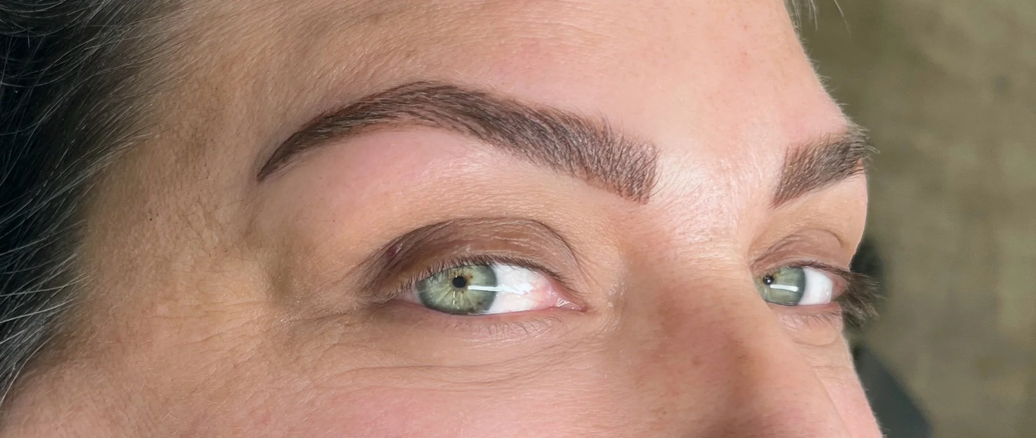 Close-up of a woman's face highlighting her well-groomed eyebrows and green eyes.