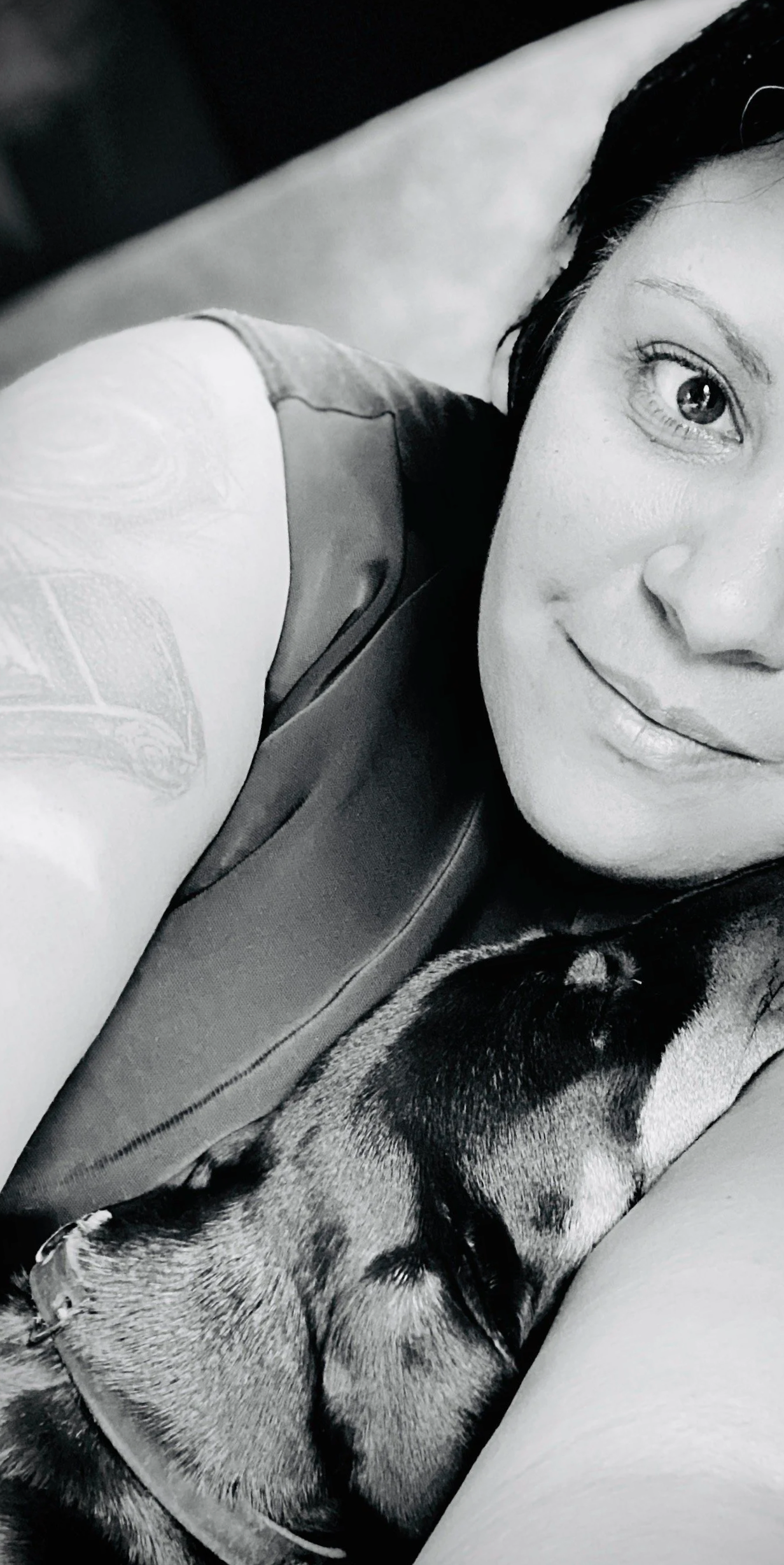 A woman with dark hair lying down next to a sleeping dog, both appearing relaxed.