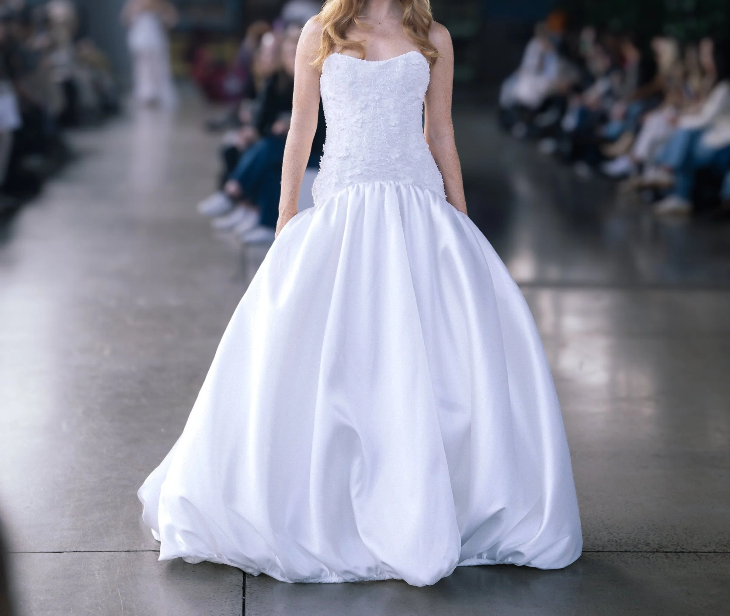 Model with red hair walks the runway in a strapless white wedding gown with a textured bodice and voluminous satin skirt.