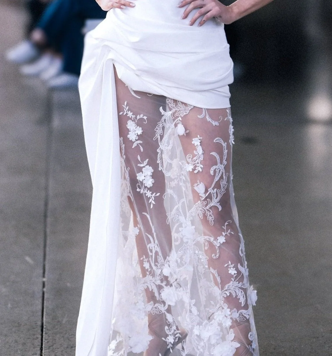 Close-up of sheer white fabric with intricate floral embroidery, part of a wedding gown worn on a runway.