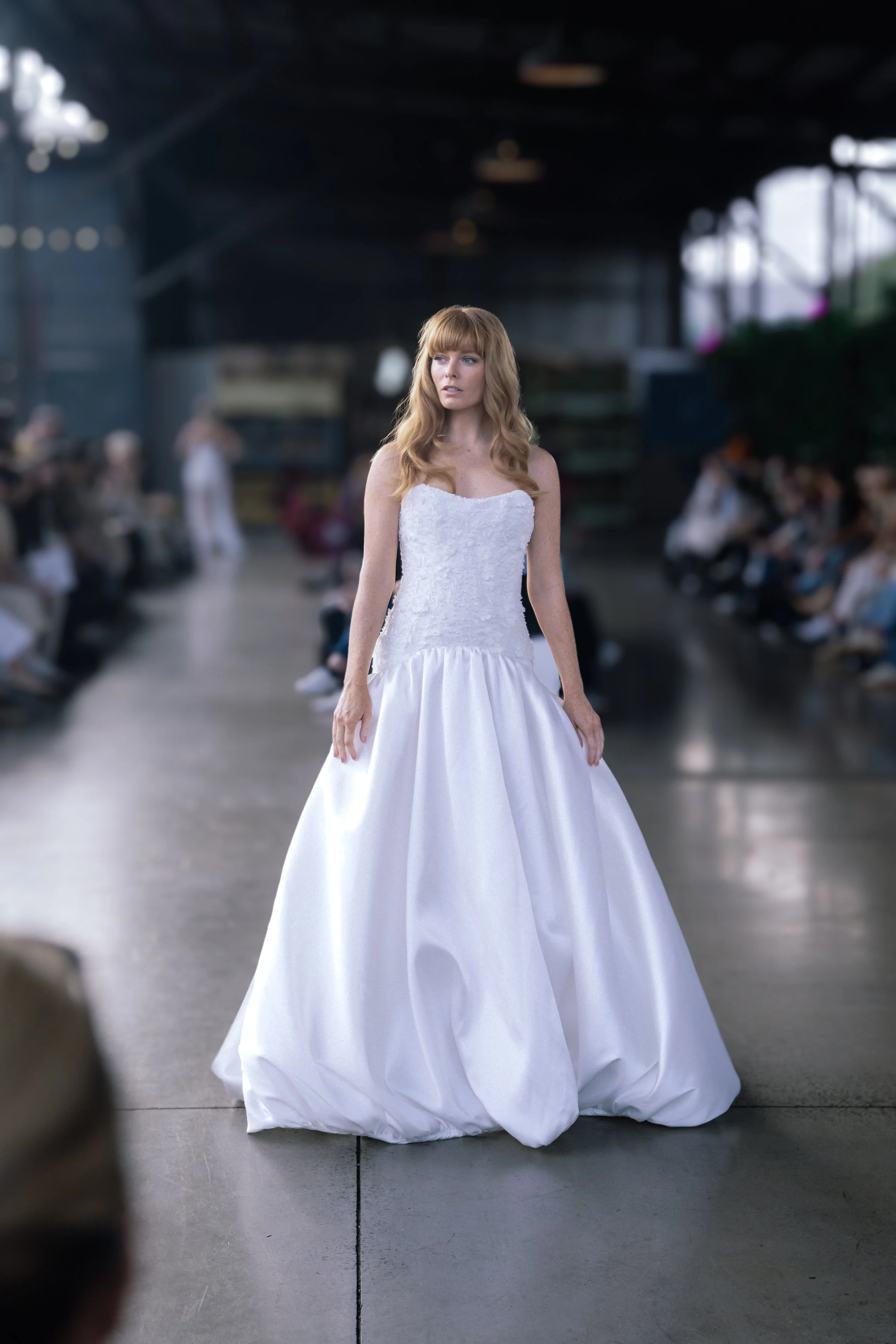 Model in a strapless textured bodice wedding gown with a voluminous satin skirt walks the runway at a bridal fashion show.