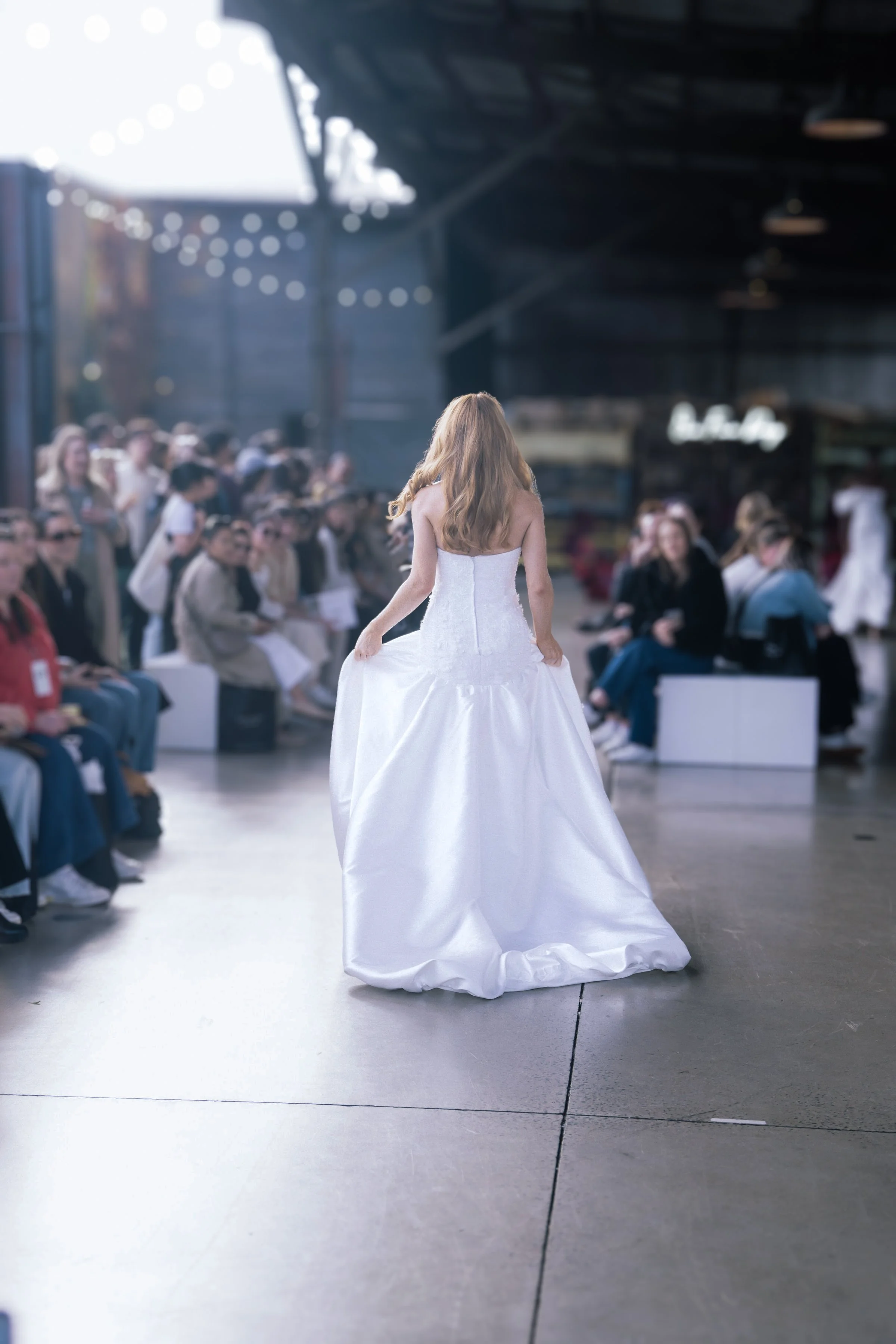 Model with long red hair walks away on the runway in a strapless white ball gown with a textured bodice and full satin skirt.