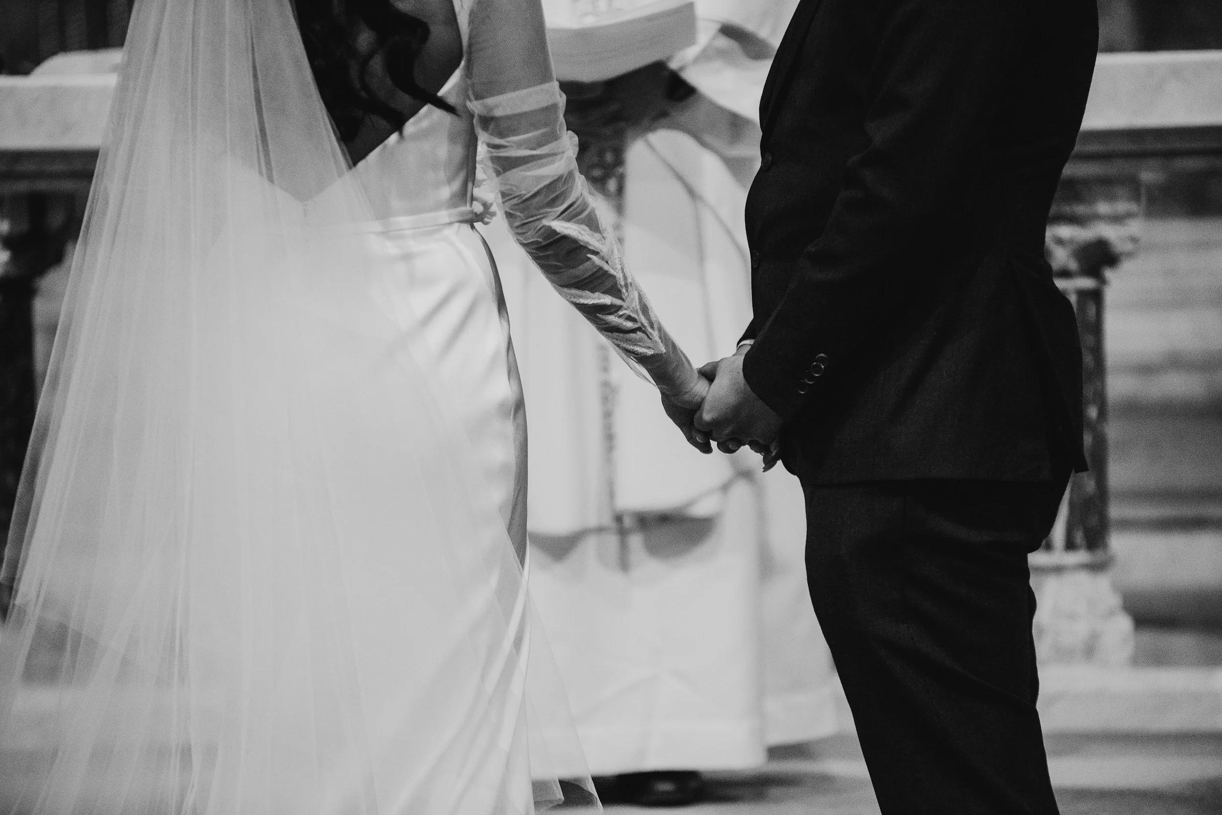 Black and white photo of a bride and groom holding hands at the altar during a wedding ceremony.
