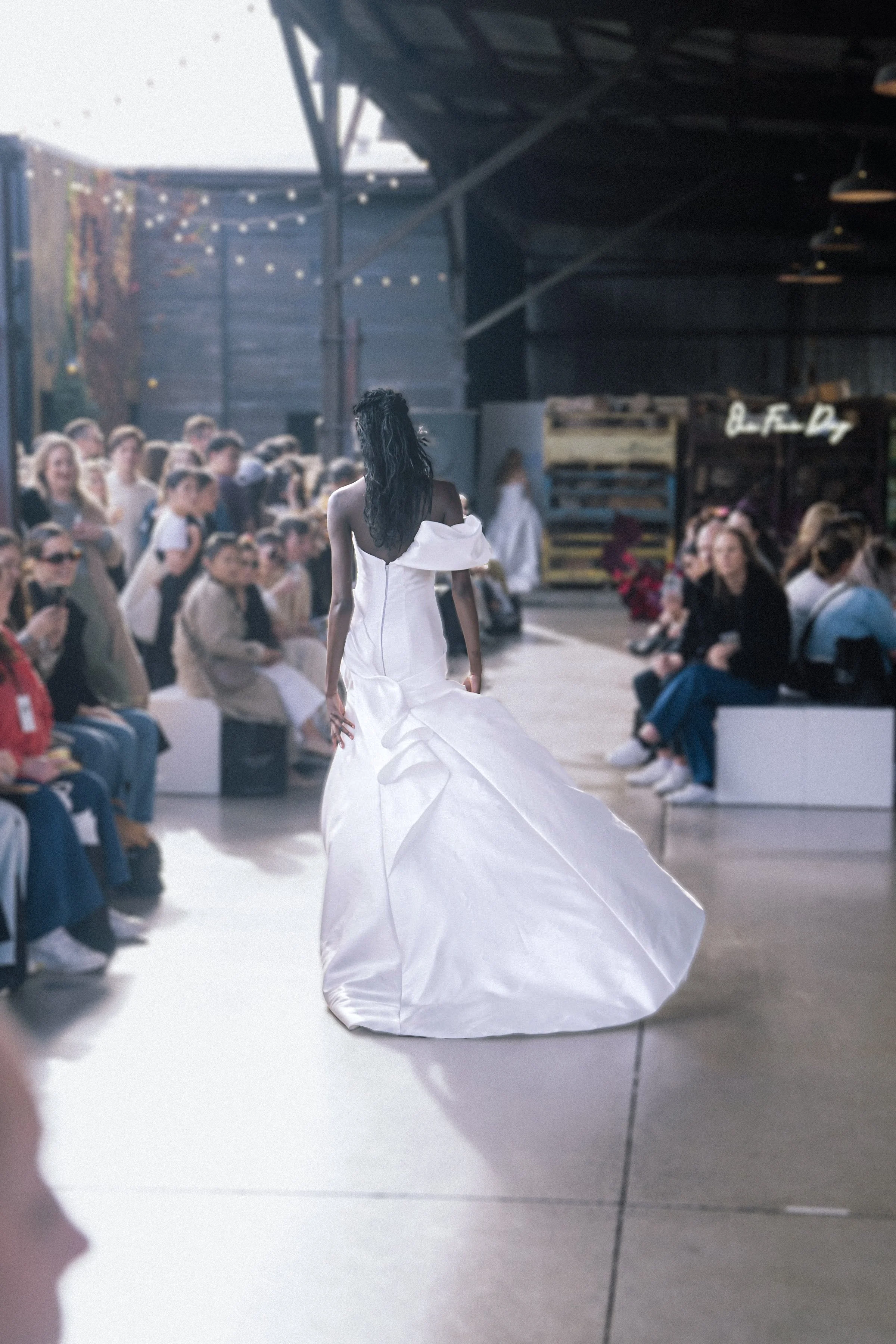 Model walks down the runway in a voluminous white gown with dramatic train and one-shoulder detail