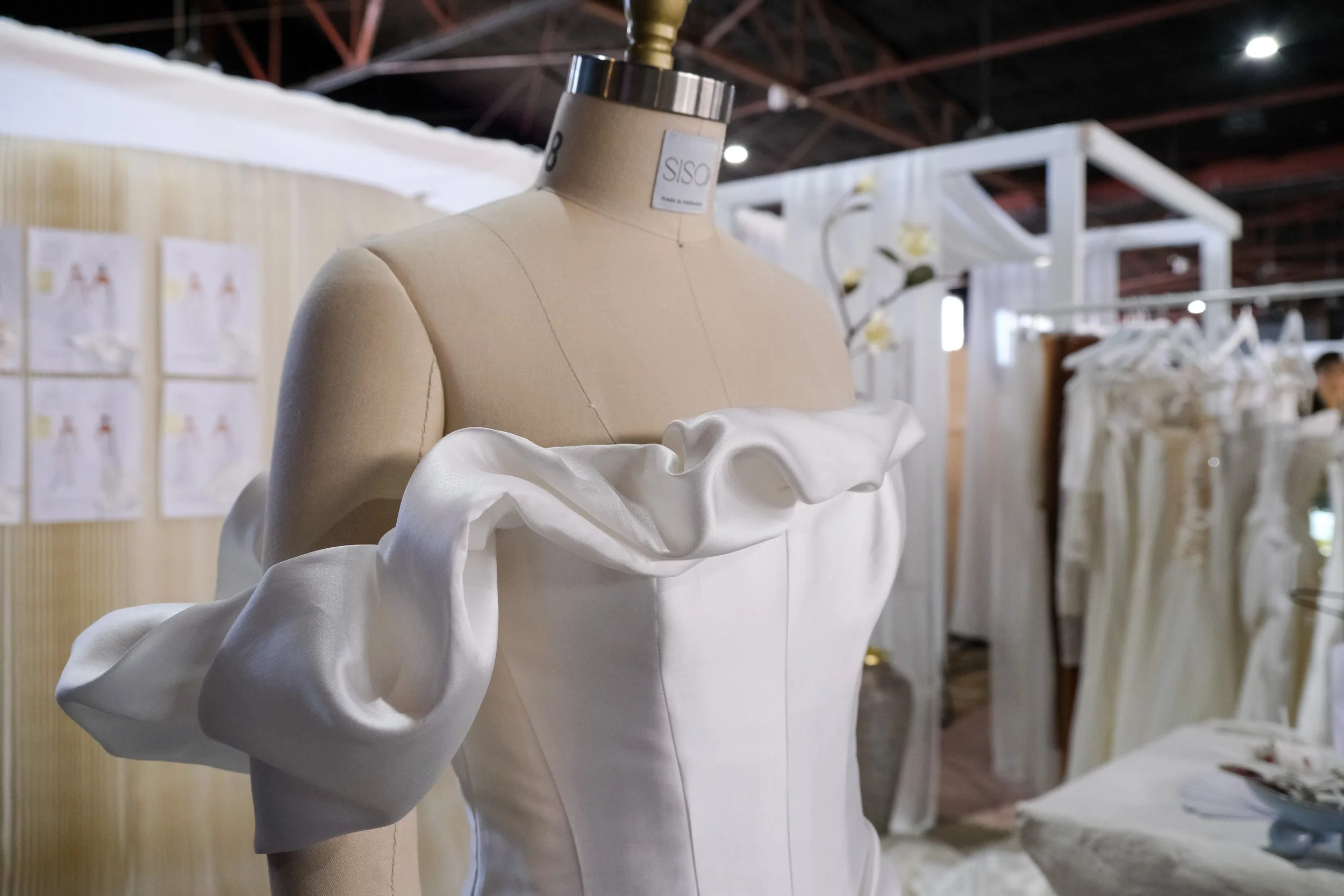 A dress on display mannequin at a fashion trade show with white fabric and ruffled sleeves.