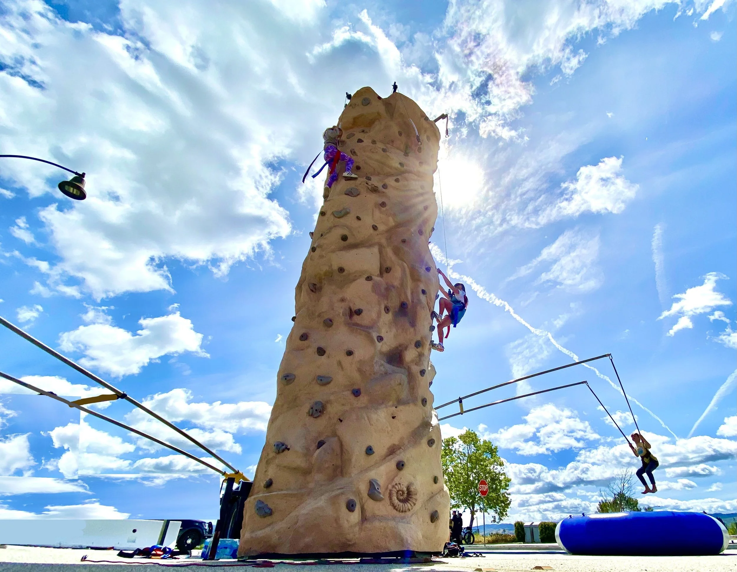 A boy climbing an inflatable military-themed obstacle course with green and camouflage designs on a sunny day.