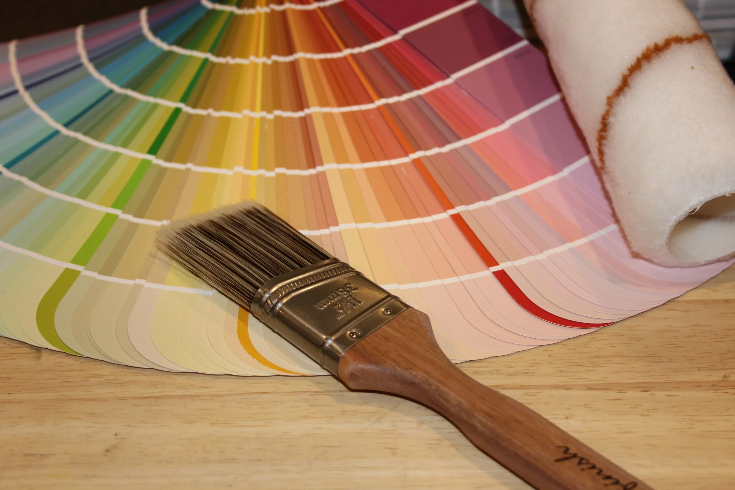 Color swatch fan, paintbrush, and paint roller on a wooden surface.