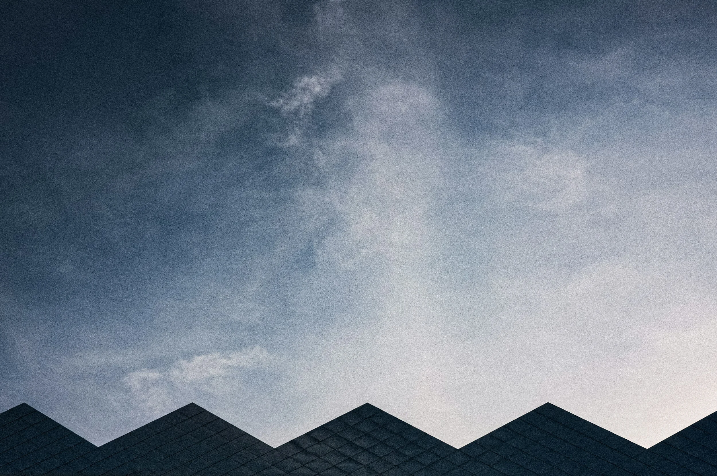 A modern building with a zigzag roofline against a partly cloudy sky at dusk or dawn.